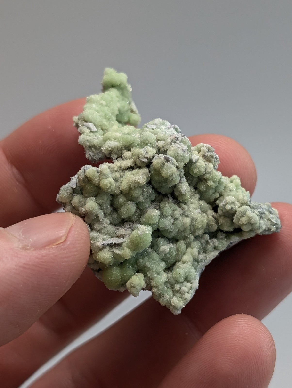 A delicate, pale green mineral specimen with a textured, bumpy surface held gently in someone’s hand.