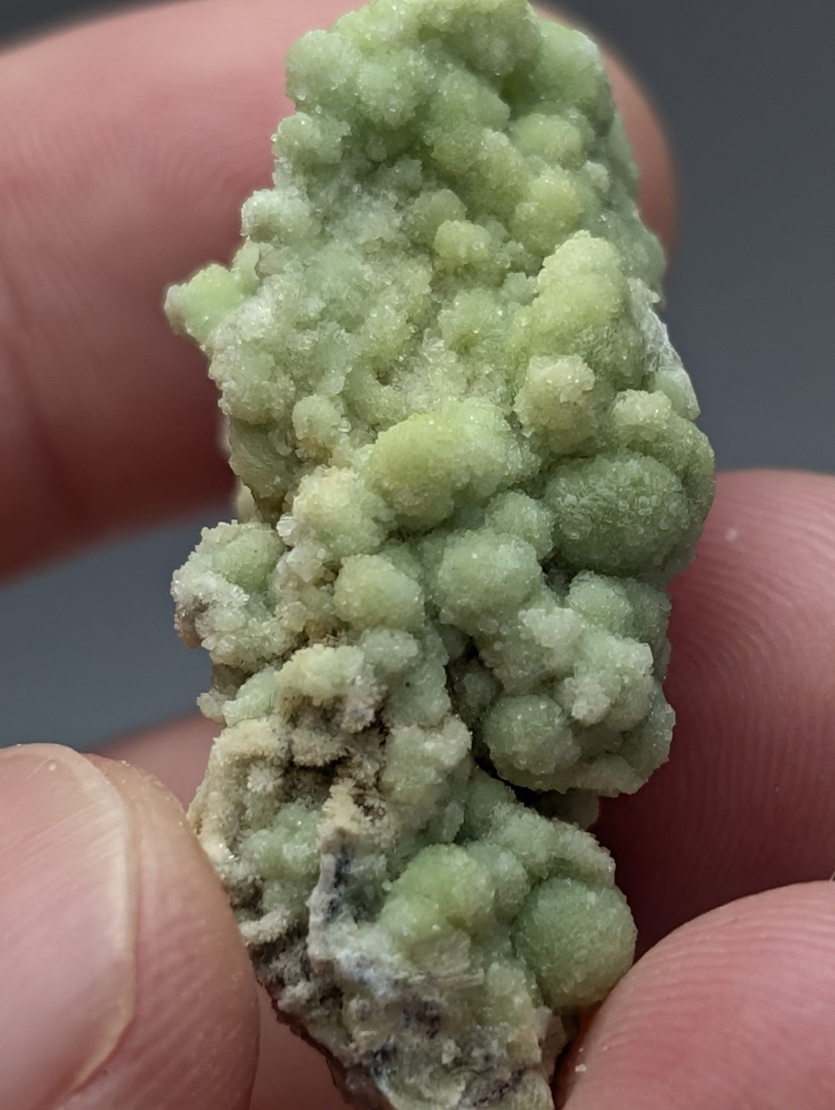 A cluster of pale green crystalline fluorwavellite intermixed with sio2 held between fingers from Mauldin Mountain Arkansas