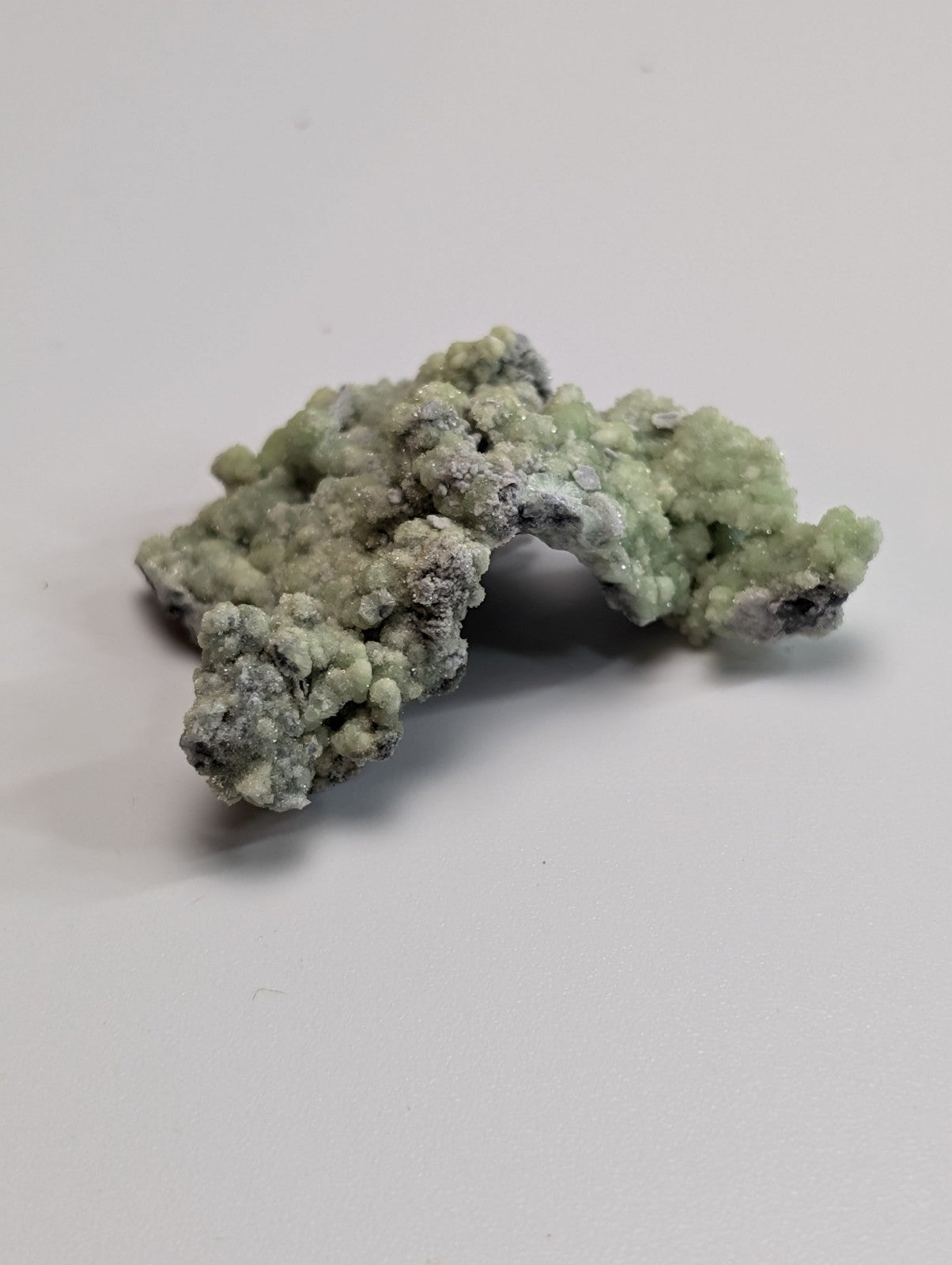 A pale green, textured mineral specimen with a rough, crystalline surface and patches of white and dark gray.