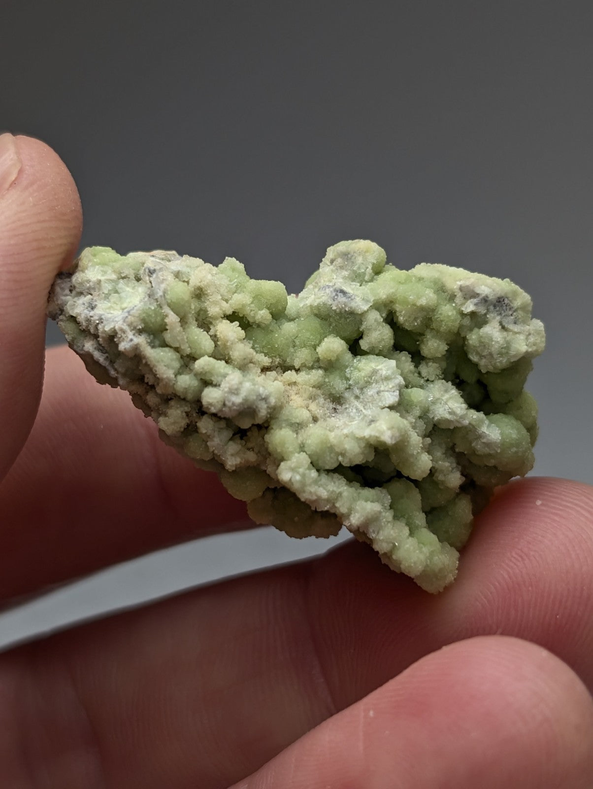 A textured light green fluorwavellite mineral specimen intermixed with sio2 held between fingers from Mauldin Mountain Arkansas