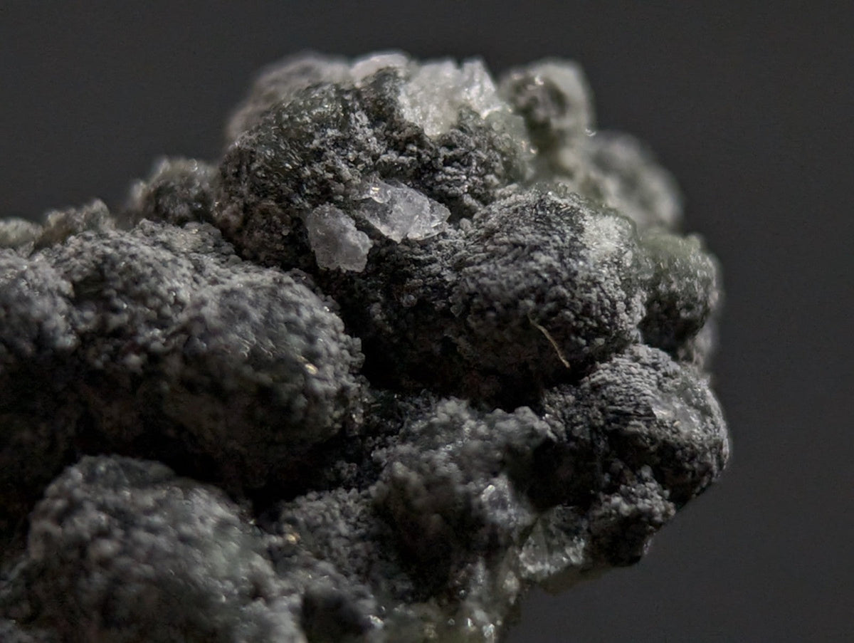 A dark gray, rough-textured mineral specimen with embedded translucent crystalline formations.