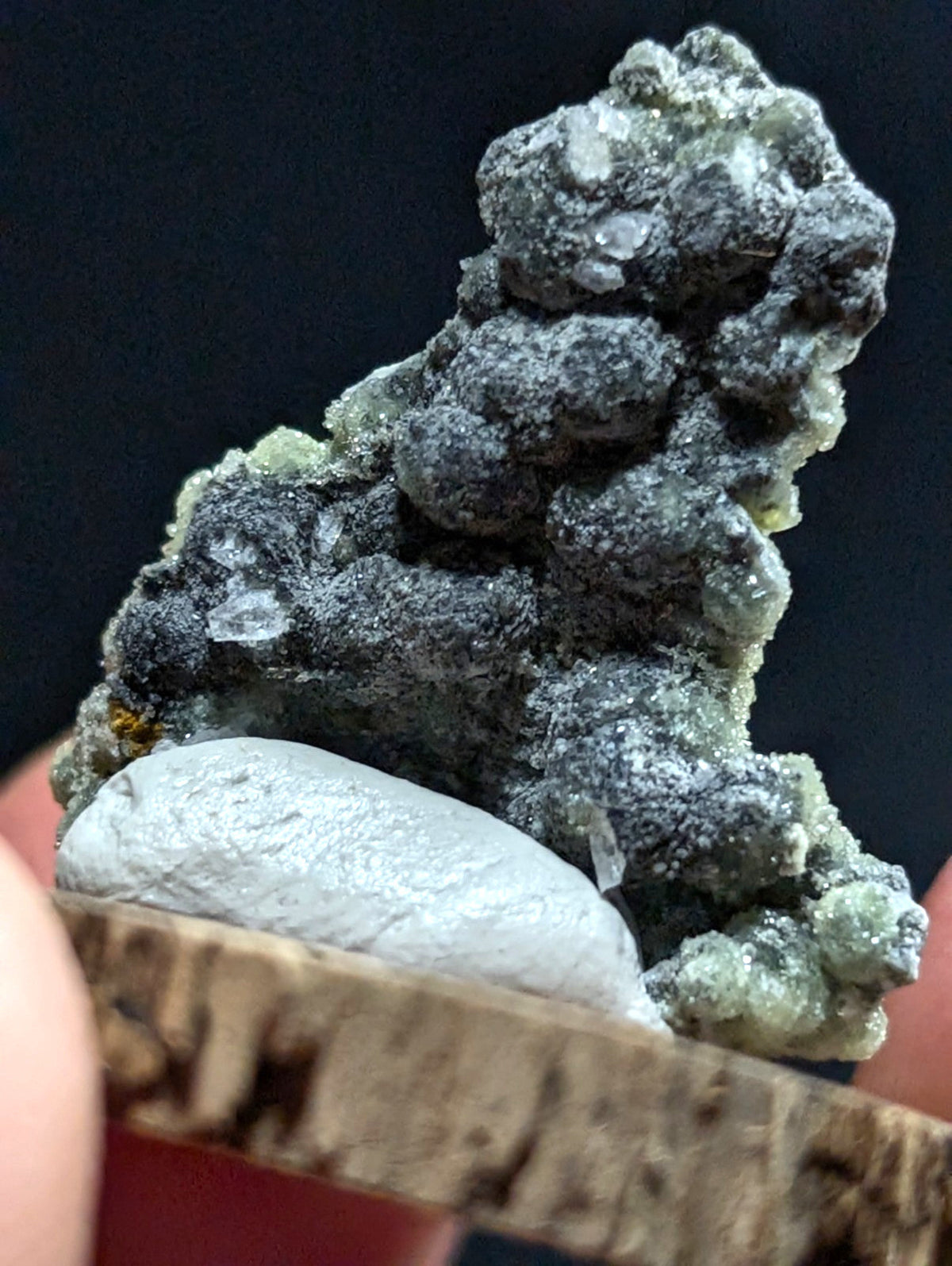 A dark gray, rough-textured mineral specimen with translucent greenish crystals growing from a lighter gray base.