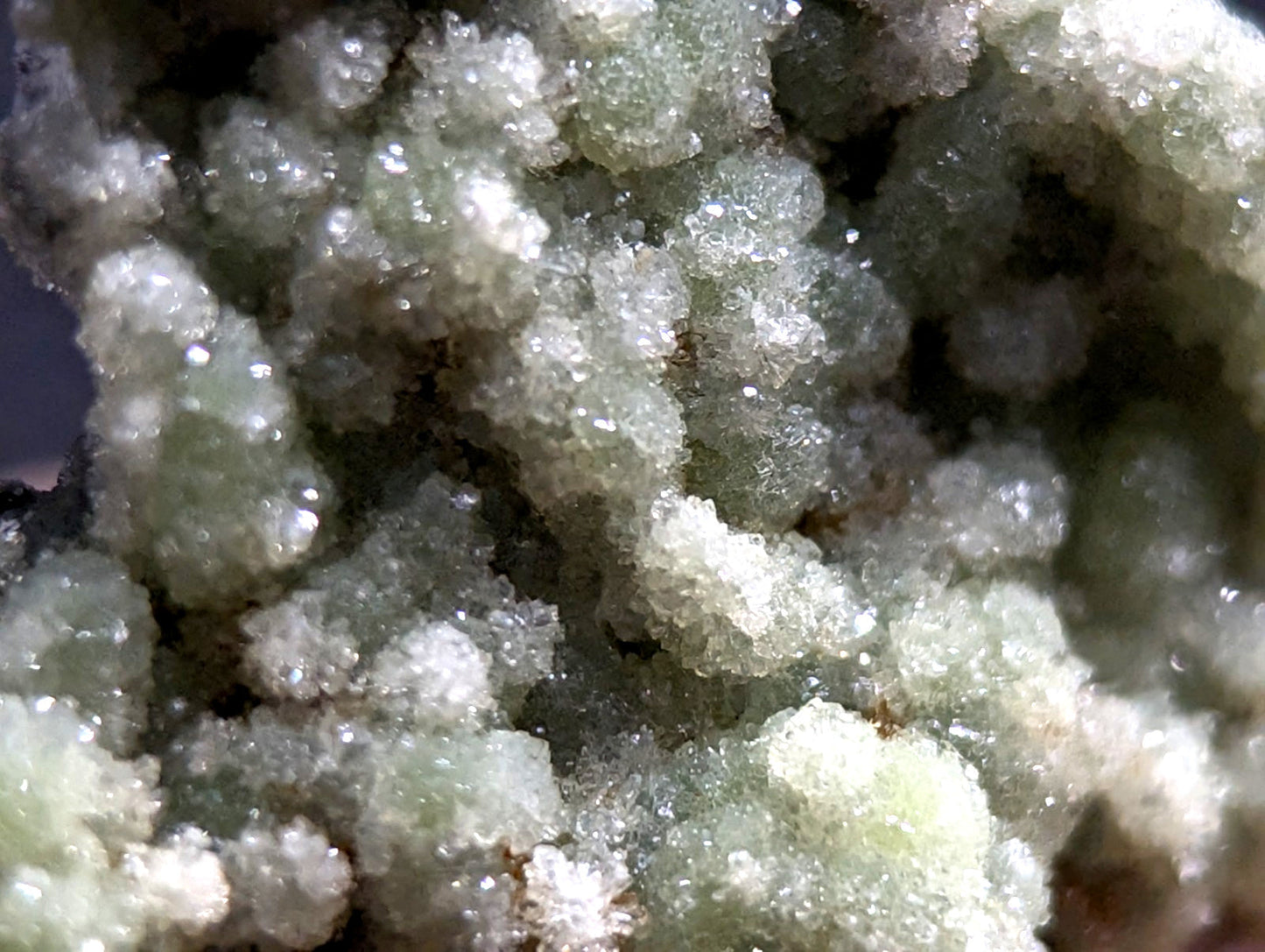 A cluster of translucent, pale green crystalline formations with a sugary texture and subtle iridescence.