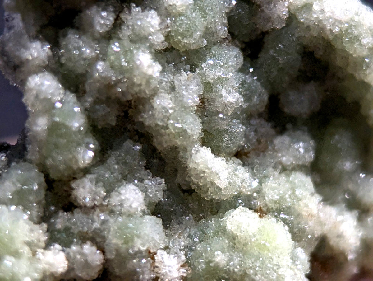 A cluster of translucent, pale green crystalline formations with a sugary texture and subtle iridescence.