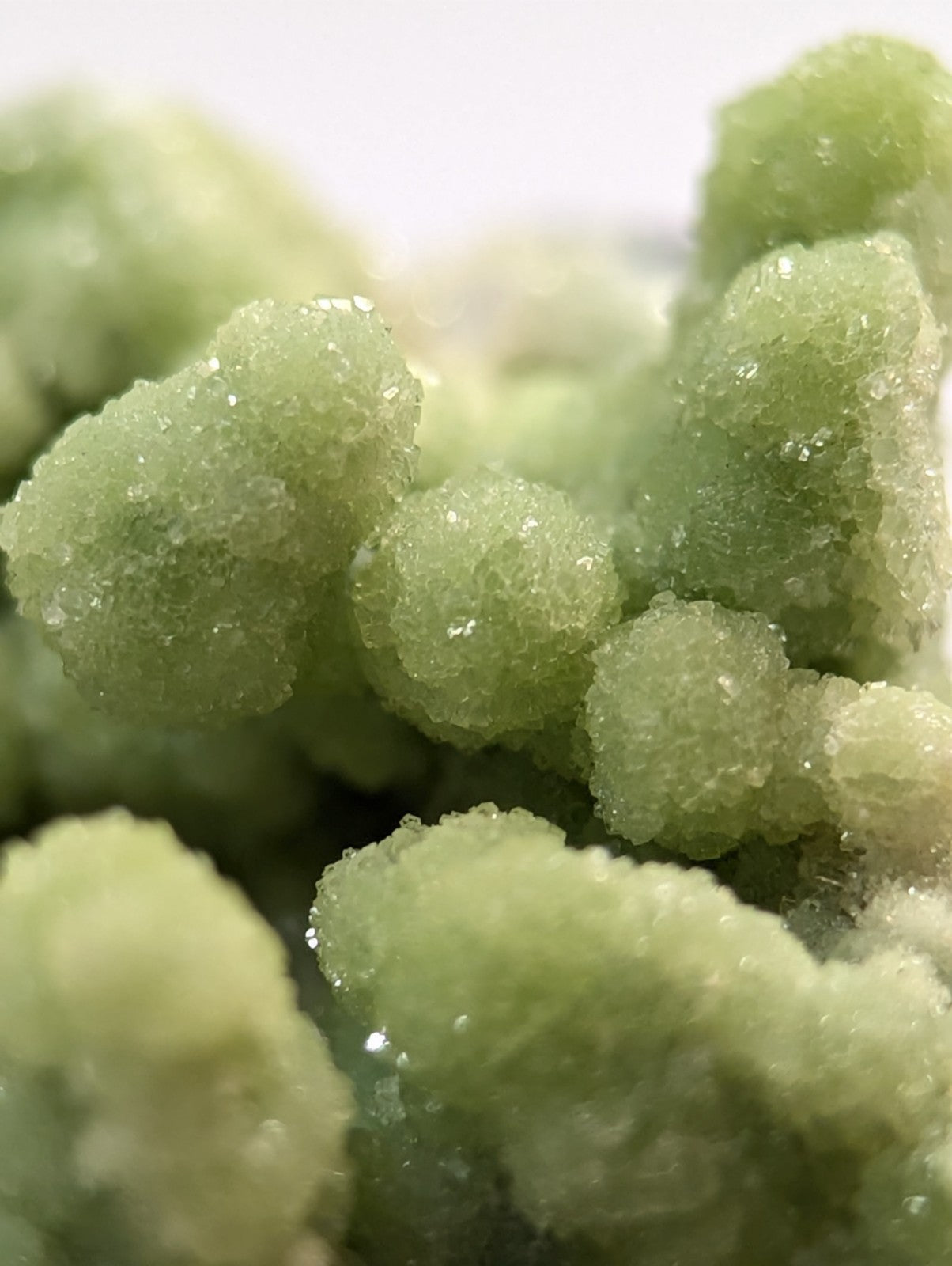 A cluster of translucent, pale green crystalline formations with a sugary texture and faceted surfaces.