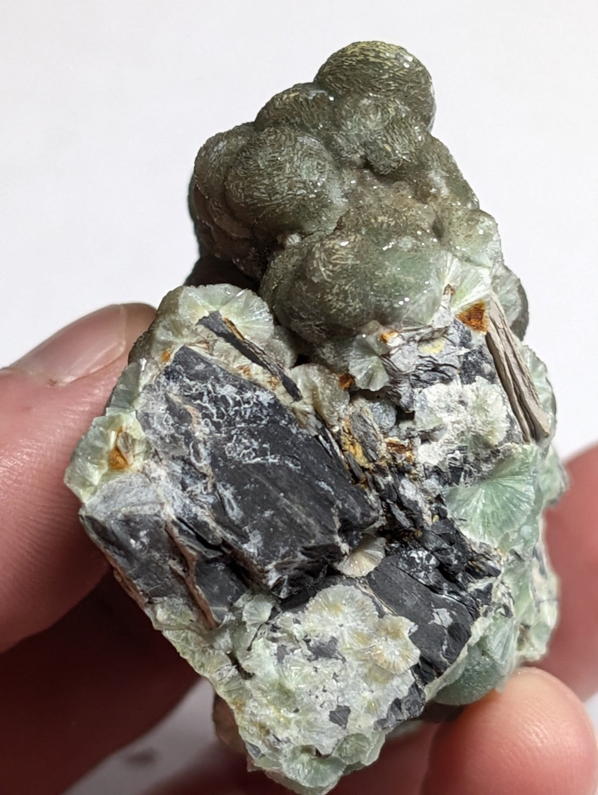 A textured, irregularly shaped mineral specimen featuring a mix of dark gray and translucent green crystalline formations with subtle orange inclusions.
