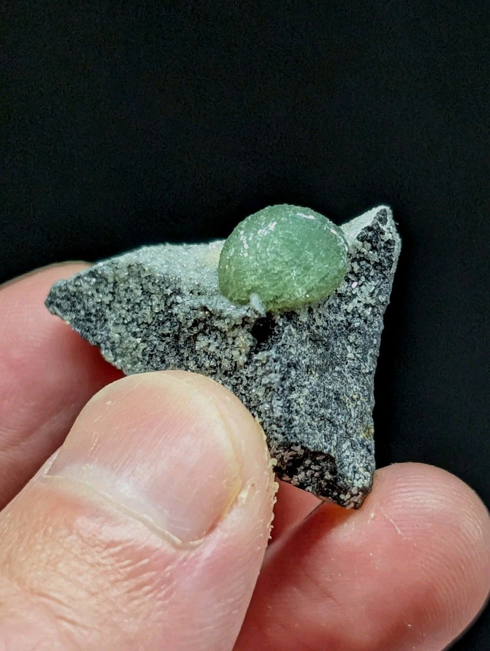 A translucent green gemstone nestled atop a speckled gray rock fragment.