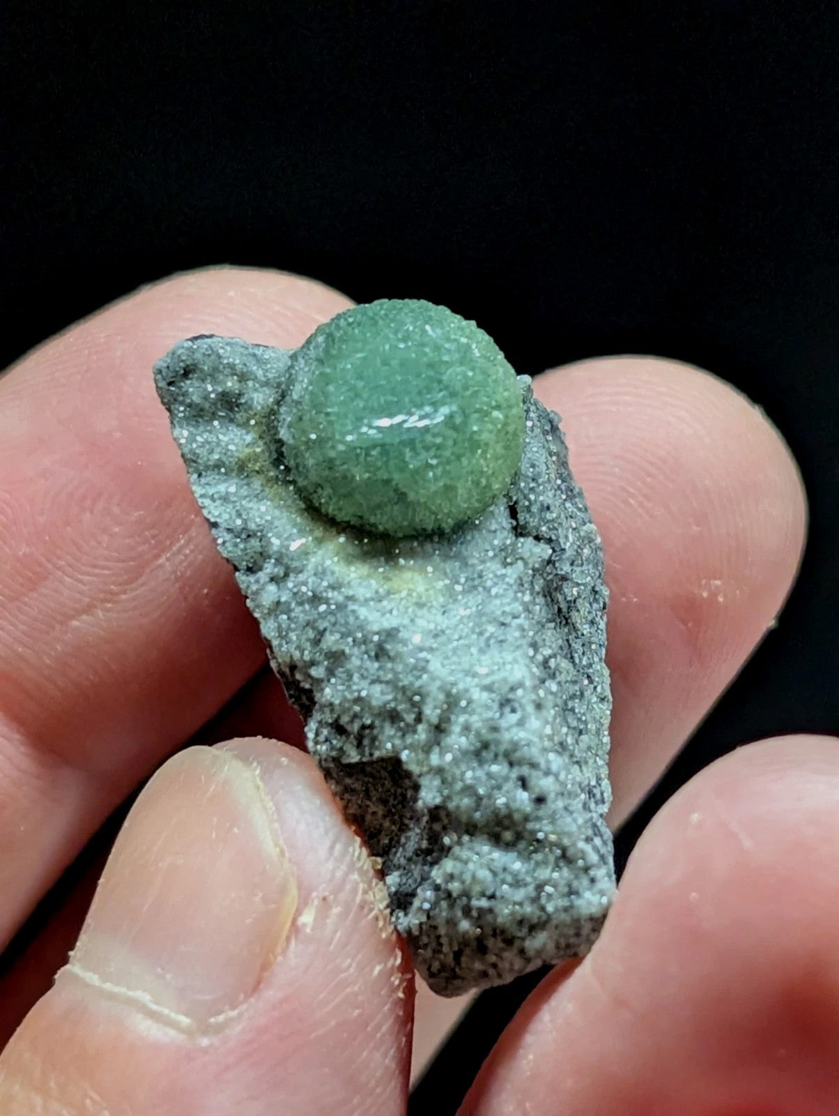 A smooth, translucent green sphere nestled atop a rough-textured gray rock.