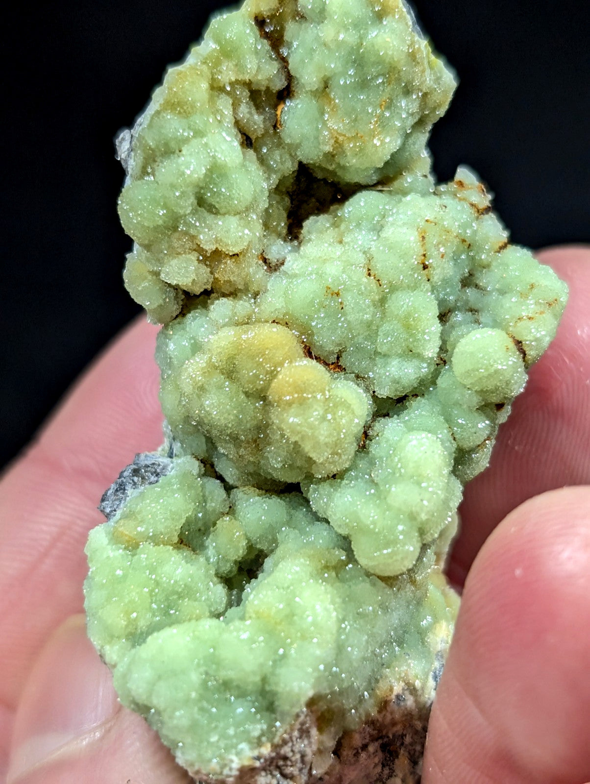 A cluster of light green, crystalline minerals with a textured, bubbly surface and hints of yellowish tones.