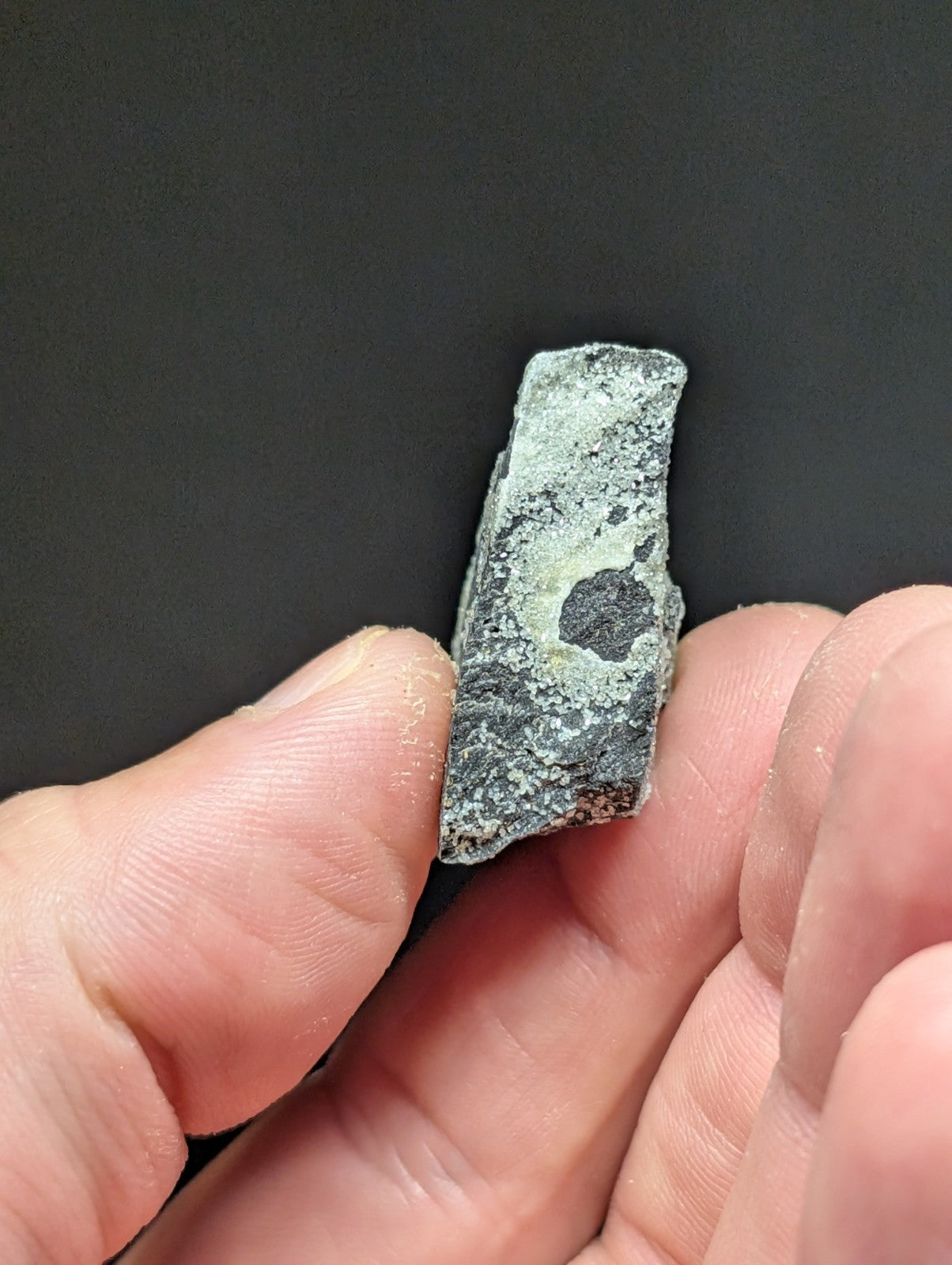 A weathered, gray-green stone fragment with a circular hole and speckled texture.