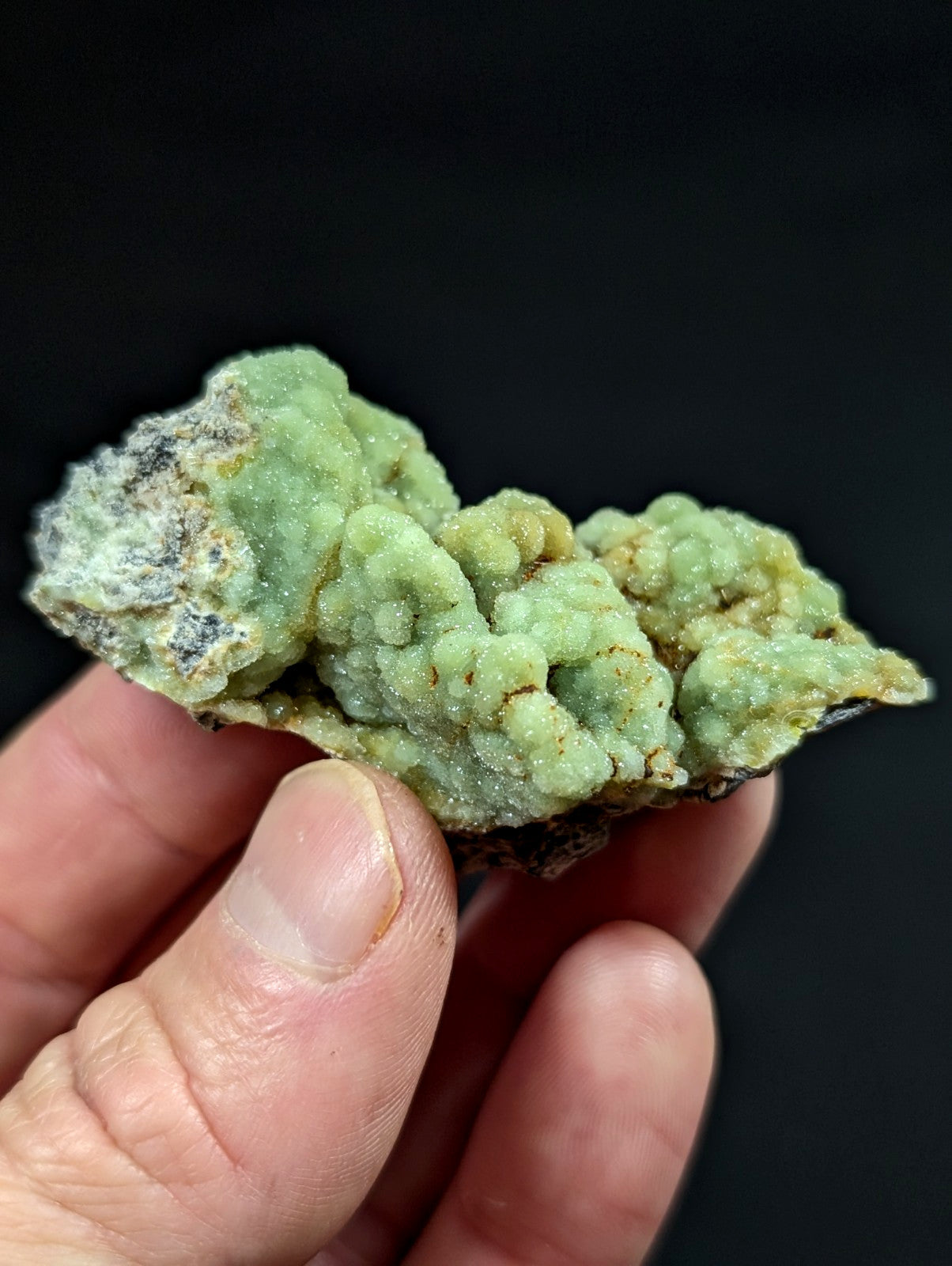 A textured, light green mineral specimen with a crystalline, bumpy surface and patches of darker earthy tones.