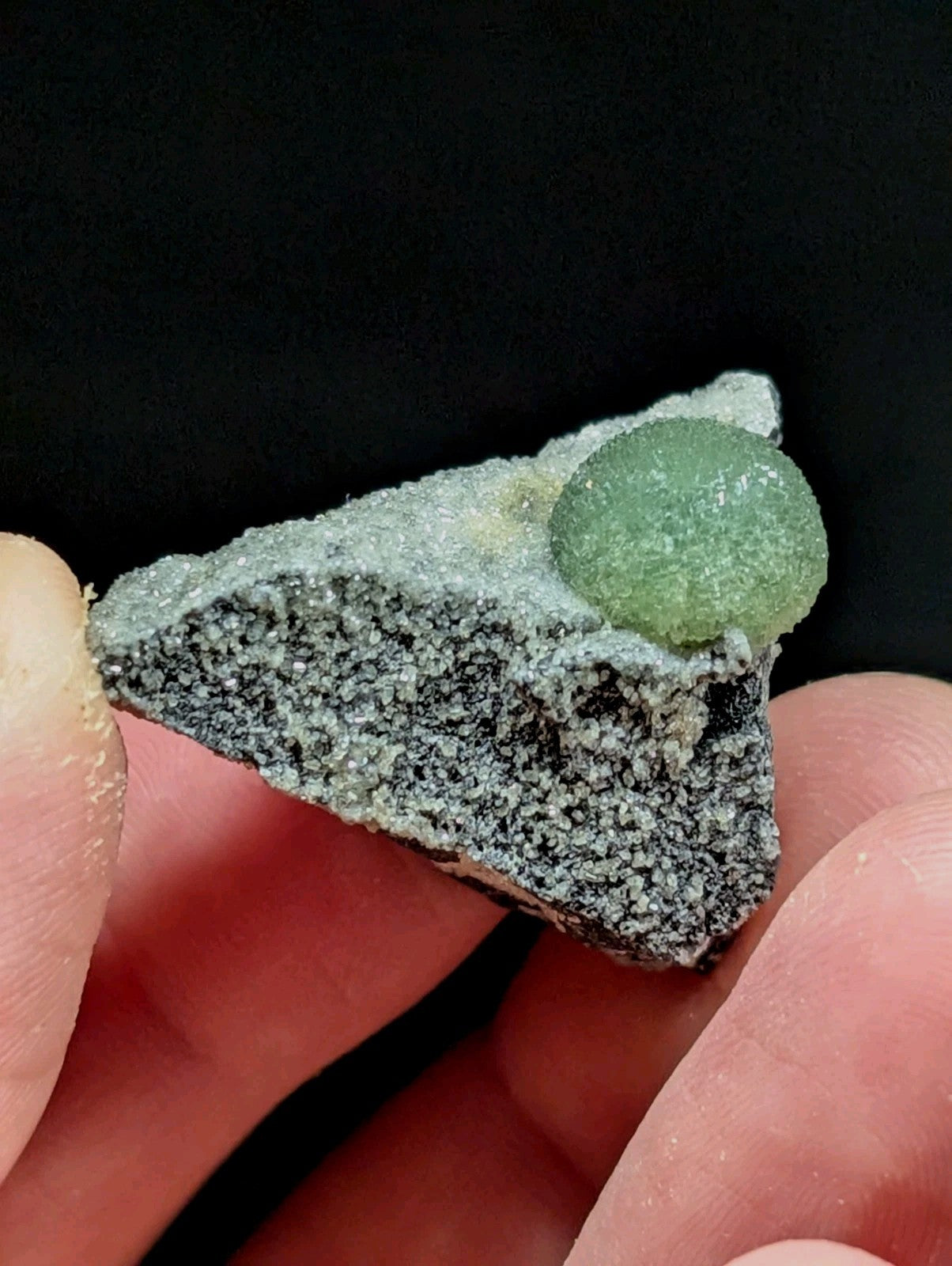 A translucent green candy sphere rests atop a textured, grayish rock fragment.