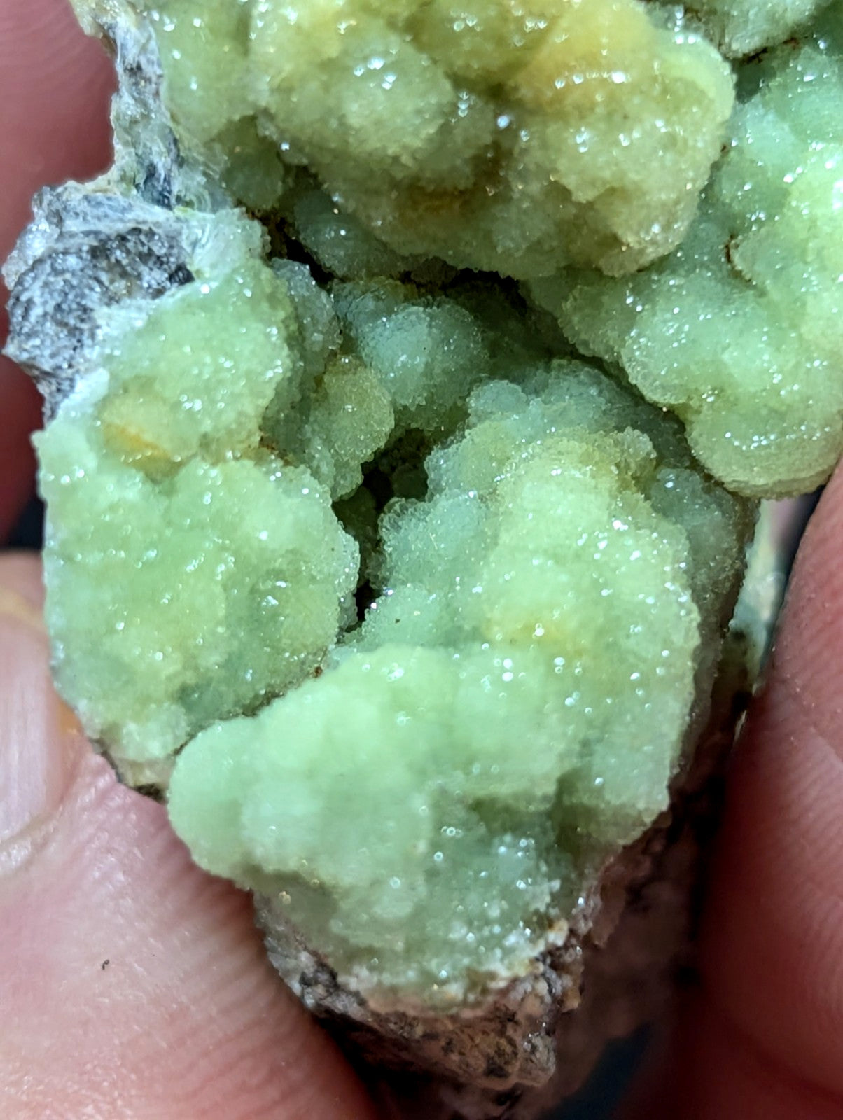A cluster of translucent, light green crystals with a crystalline texture and subtle yellowish highlights.