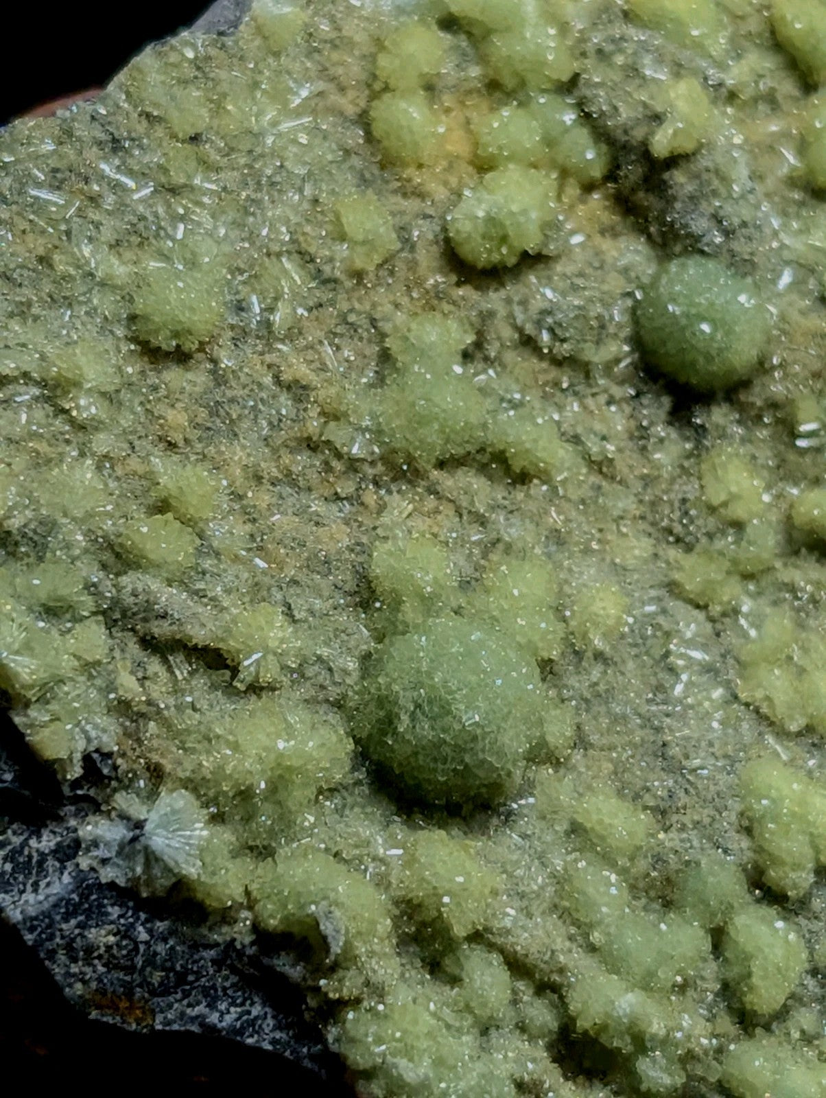 A cluster of translucent, pale green crystals with a rough, textured surface and small spherical formations.