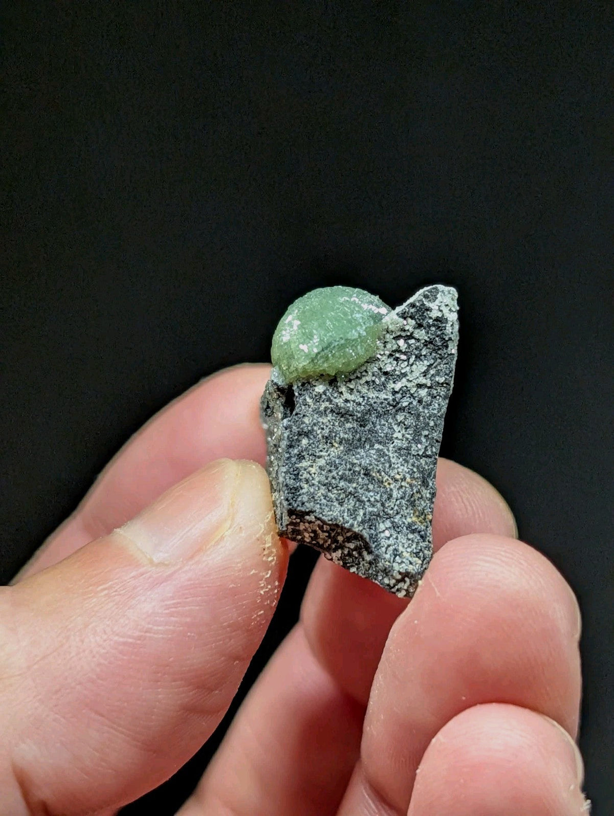 A smooth, translucent green jade stone nestled atop a rough-textured gray rock fragment.