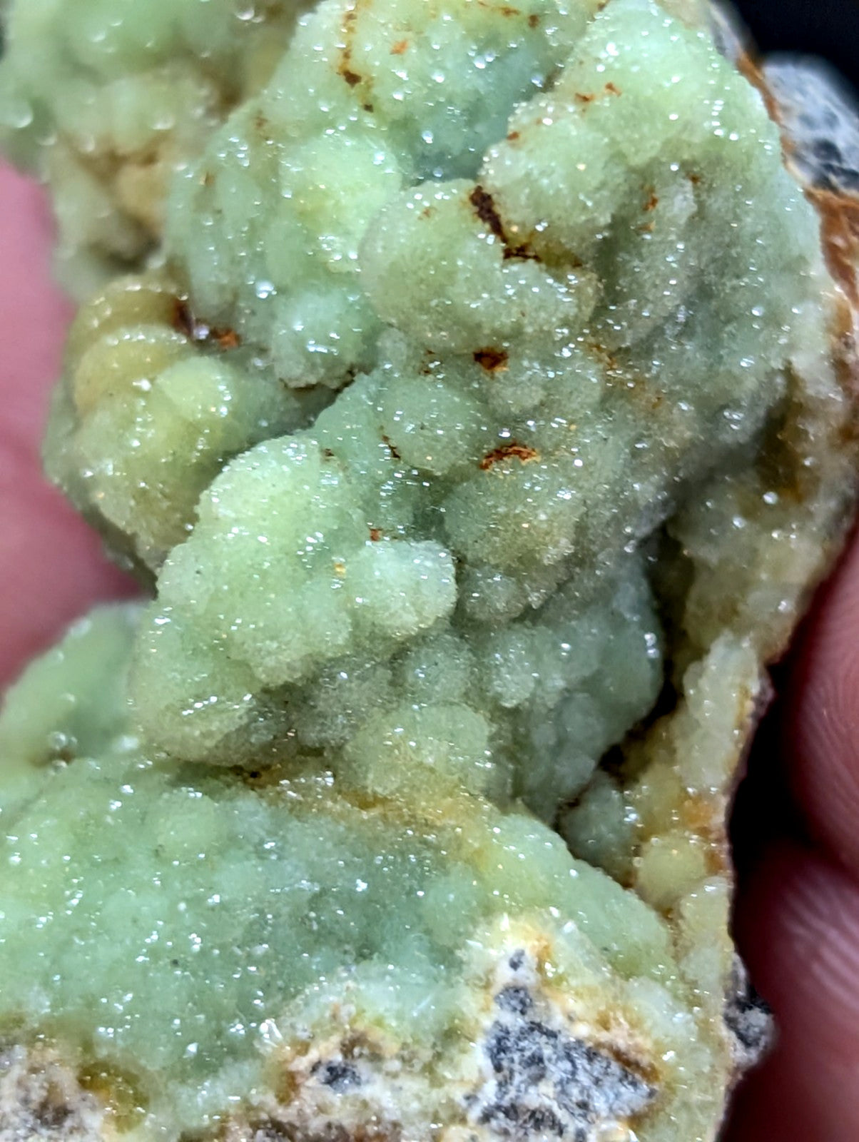 A pale green, crystalline mineral specimen with a textured, bubbly surface and hints of yellowish-brown veining.