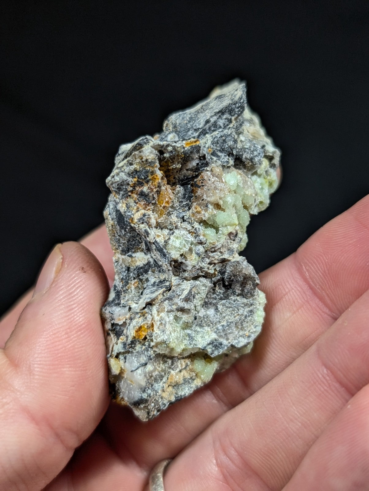 A rough, irregularly shaped mineral specimen with a mottled green and gray surface accented by patches of orange-yellow.