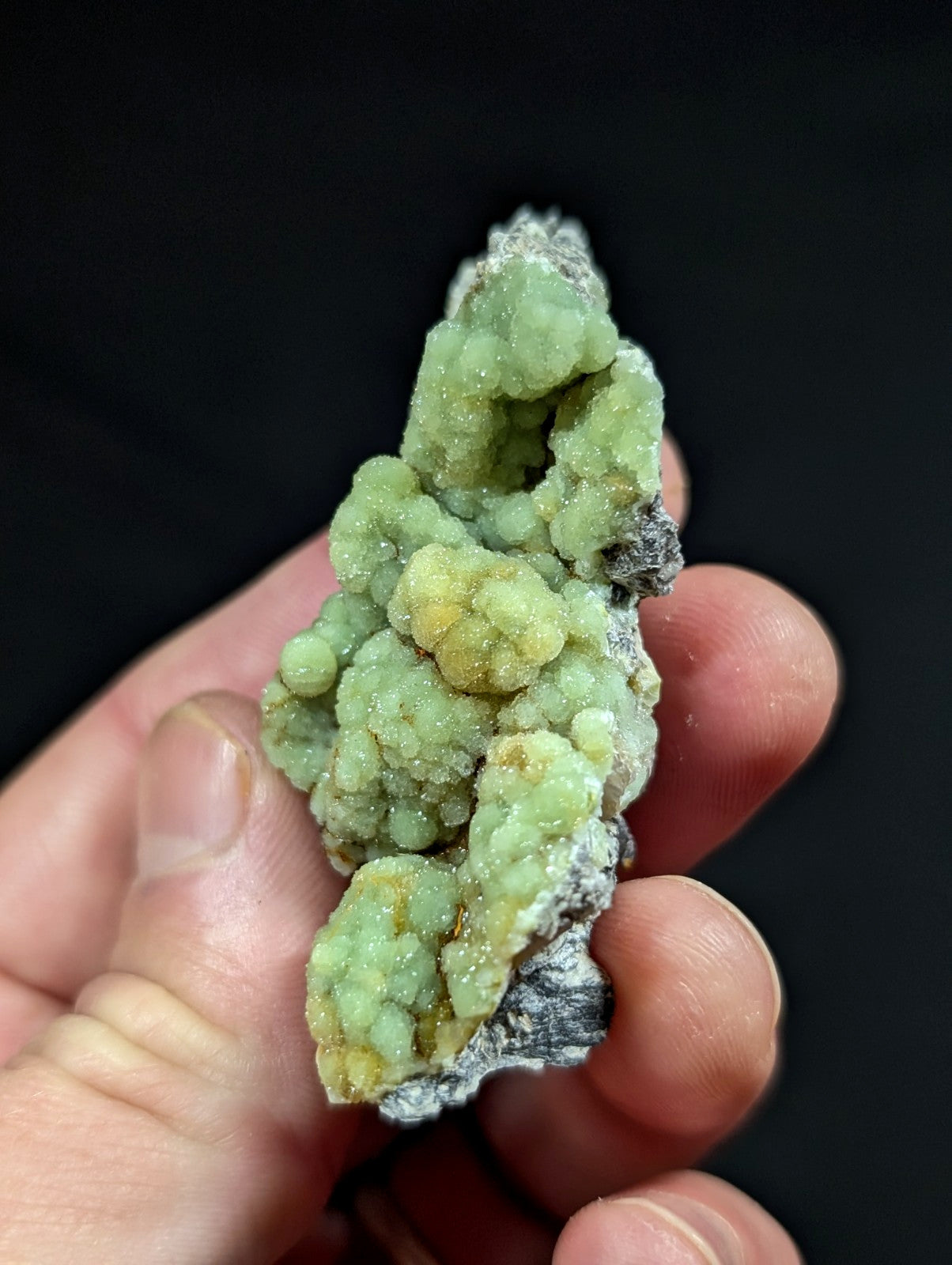 A hand holds a striking green and yellow mineral specimen with a textured, crystalline surface.