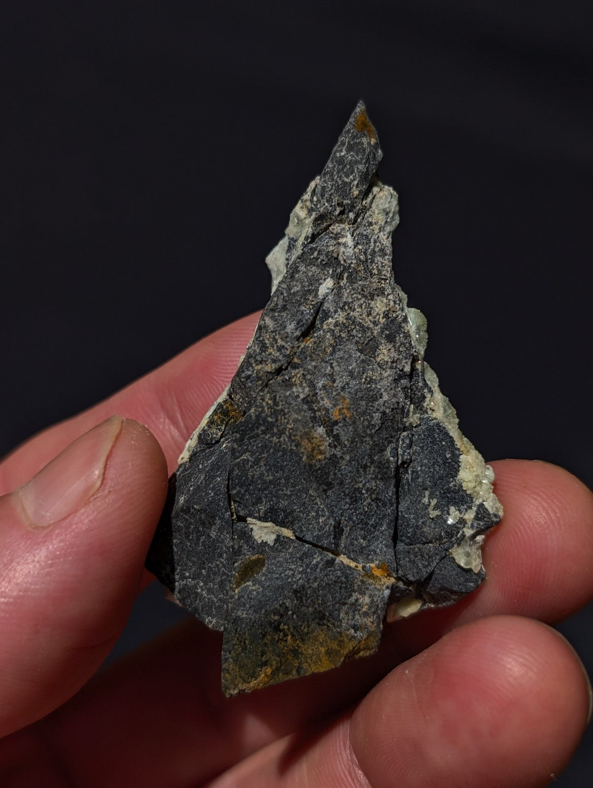 A dark gray, irregularly shaped rock fragment with patches of yellow and white mineral streaks.