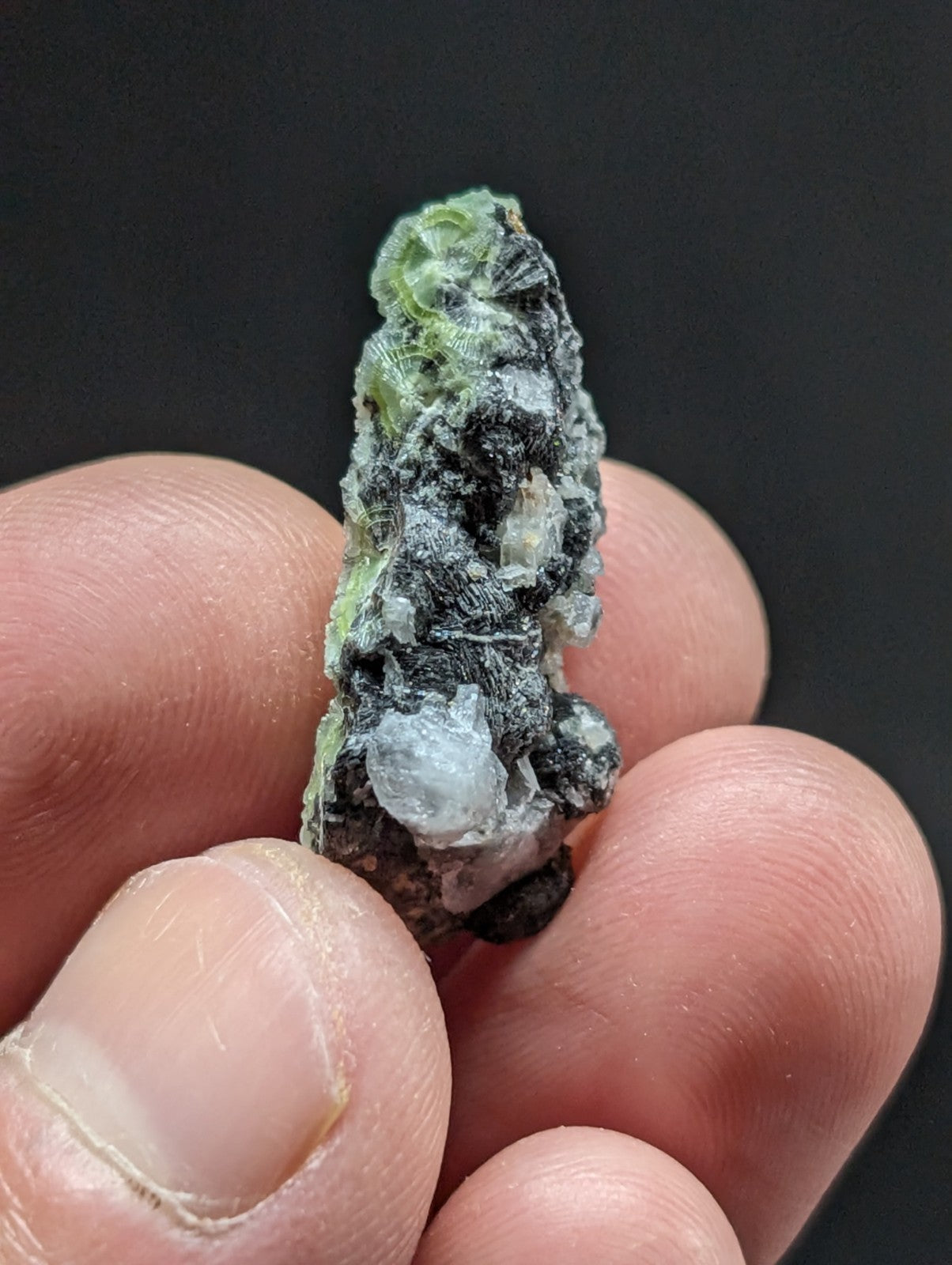 A rough, irregularly shaped mineral specimen with a mix of dark gray and translucent green crystalline formations.