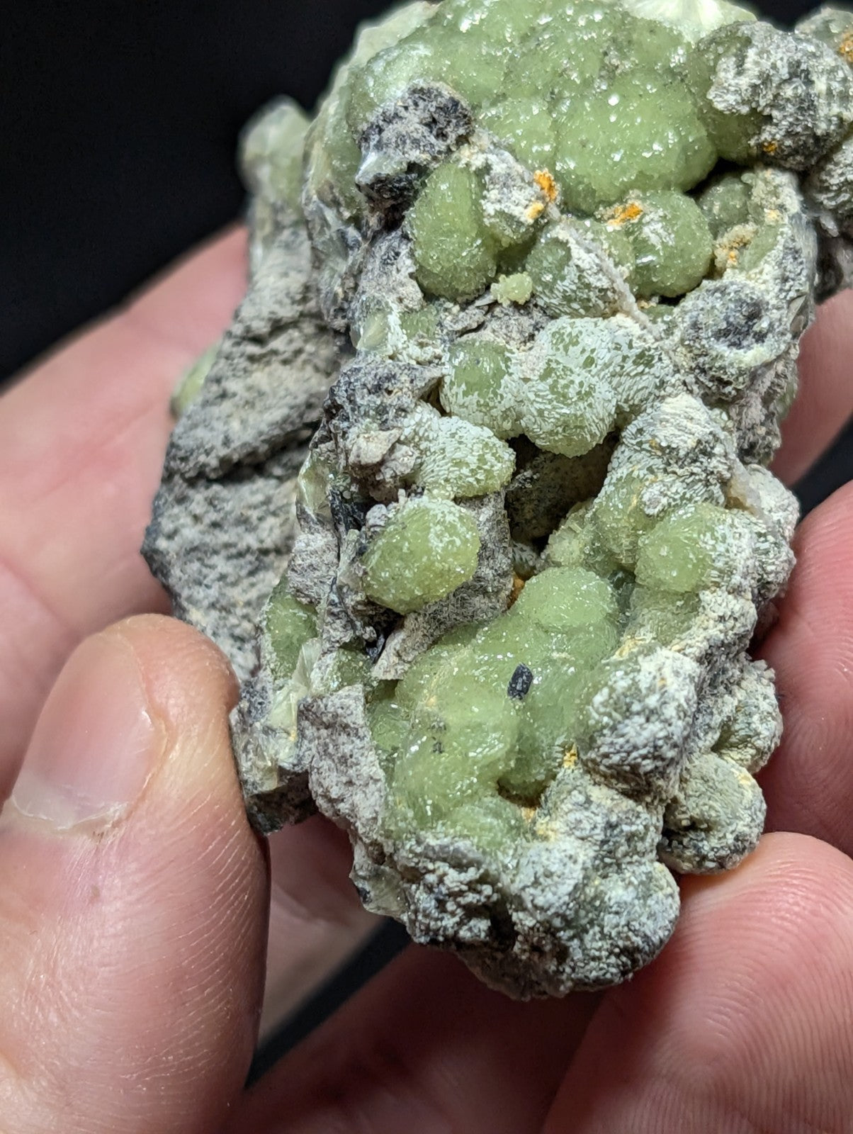 A hand holds a cluster of translucent green gemstones embedded in a gray, rocky matrix.
