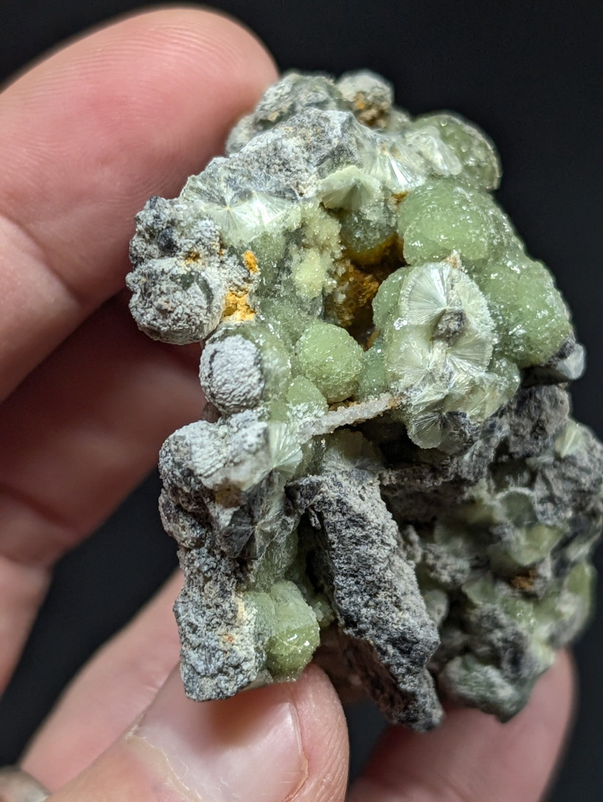 A hand holds a cluster of translucent green and gray mineral crystals with some yellowish inclusions.
