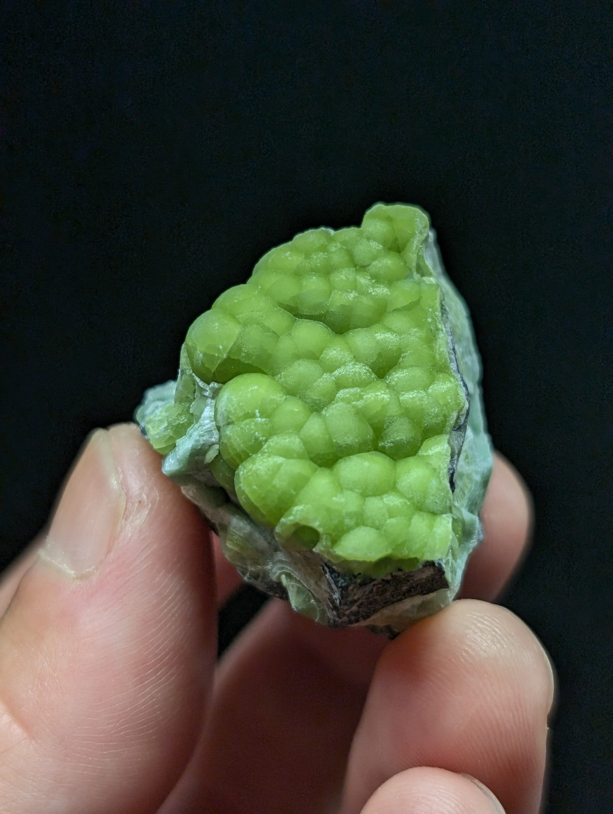A vibrant lime-green, bumpy mineral specimen with a rough, crystalline texture and grayish matrix.