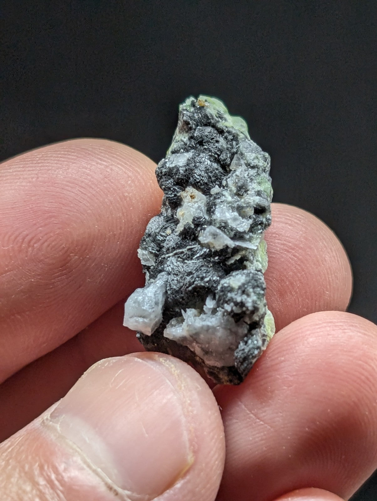 A rough, irregularly shaped mineral specimen with a mix of dark gray and pale greenish-white crystalline formations.
