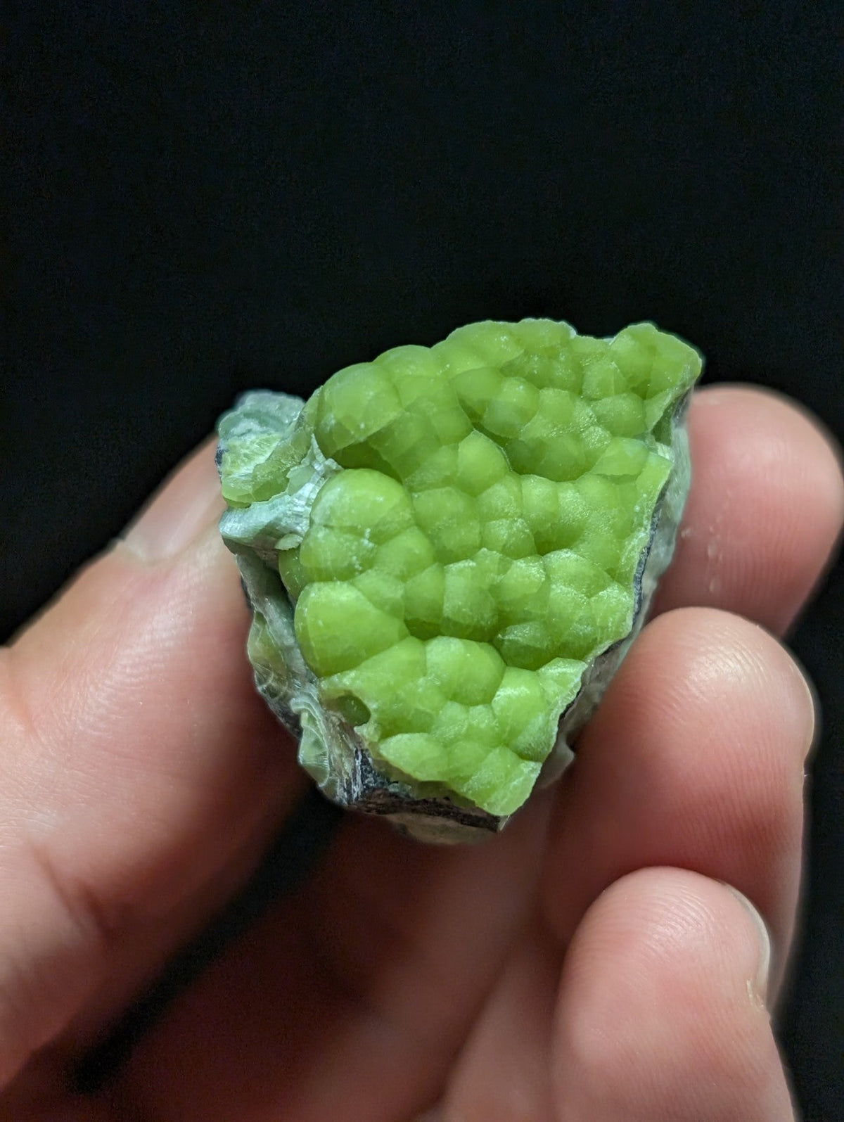 A vibrant lime-green mineral specimen with a clustered, bumpy surface texture and some grayish matrix material.