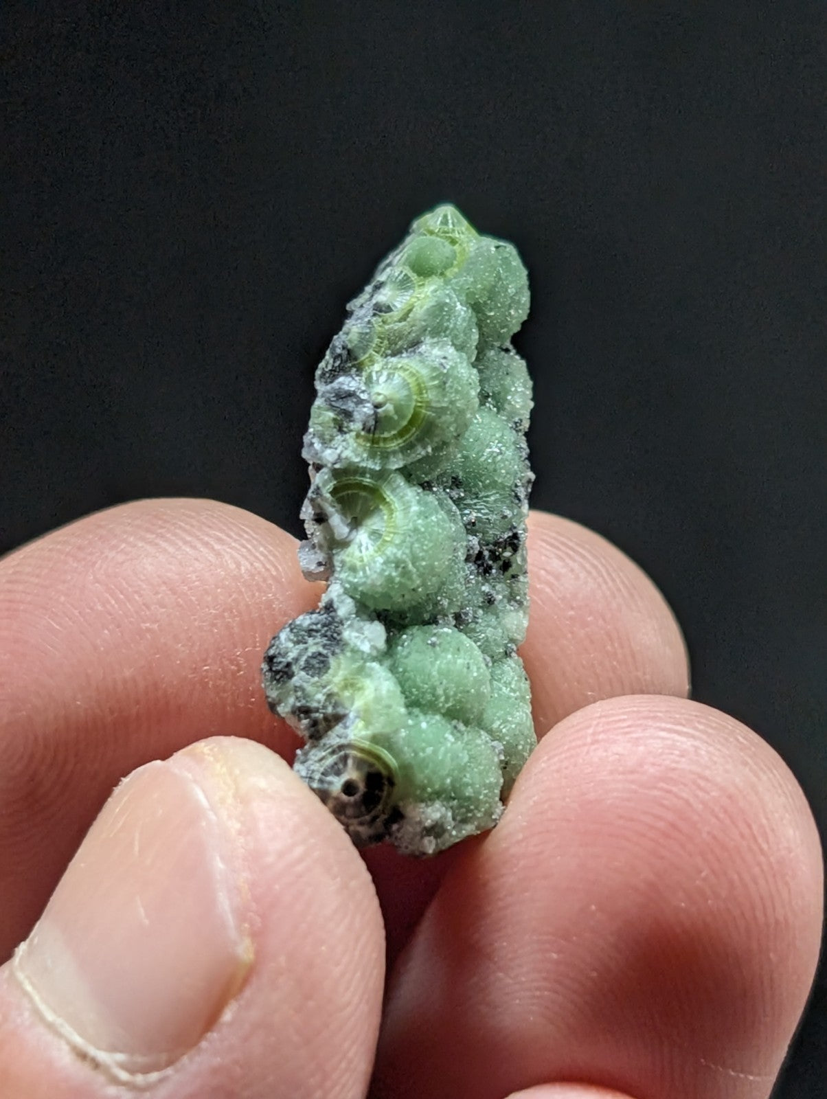 A cluster of small, greenish mineral formations with a rough, textured surface and dark speckles.