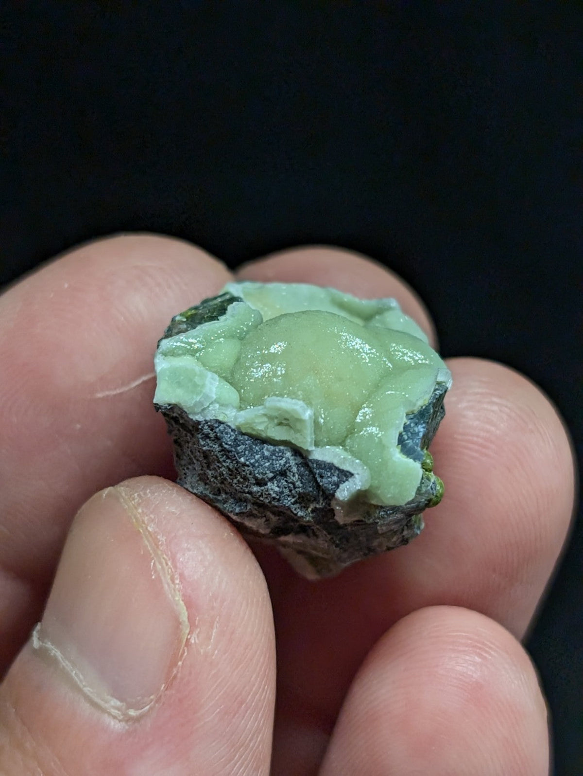 A smooth, light green jade-like stone with a glossy surface and irregular edges, set against a dark background.