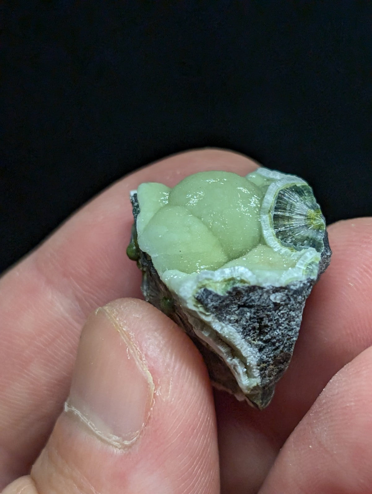 A translucent green mineral specimen with a smooth, rounded interior and rough, dark gray exterior.
