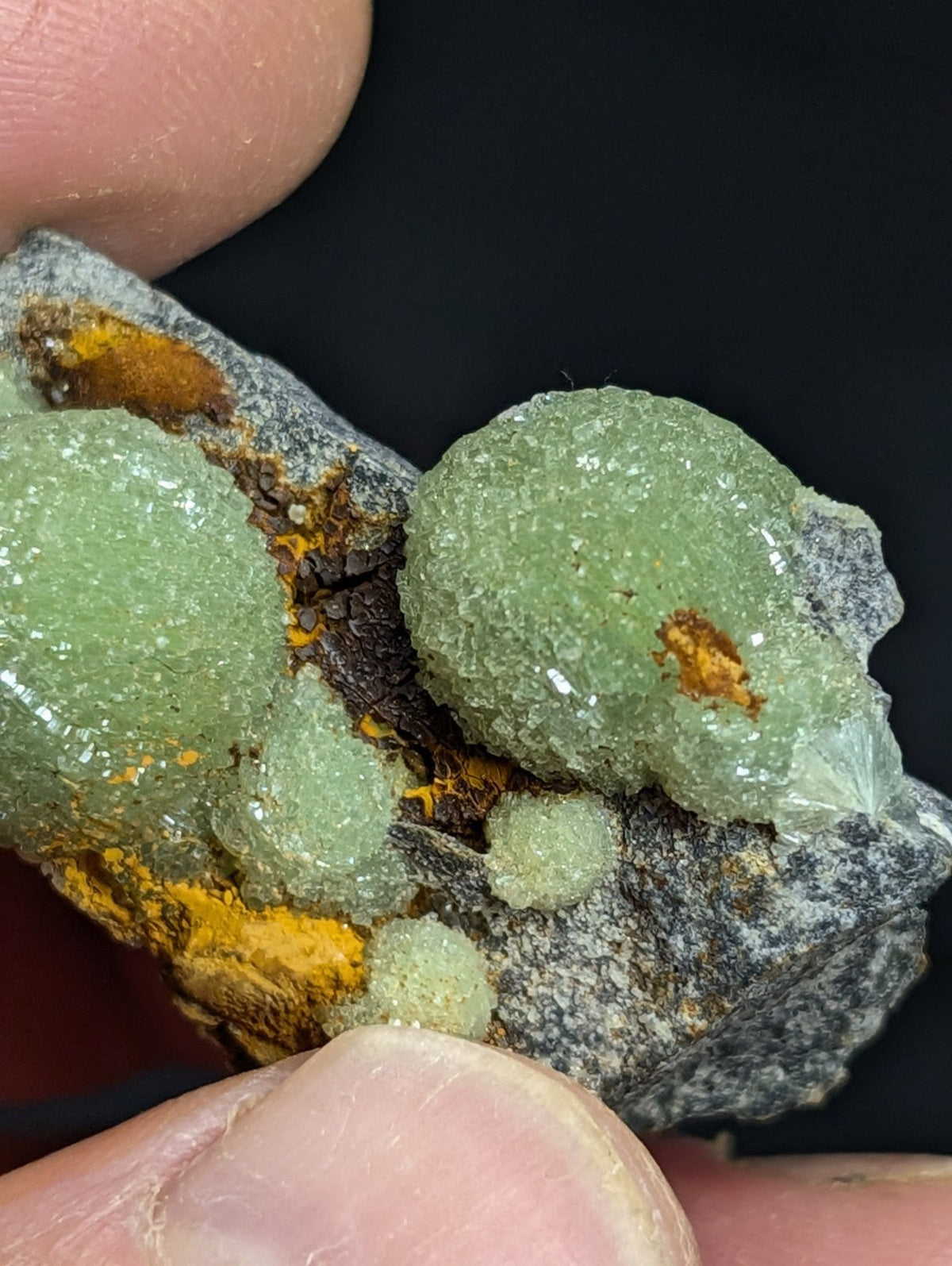 A cluster of translucent green crystals with a rough, textured surface and orange mineral inclusions.