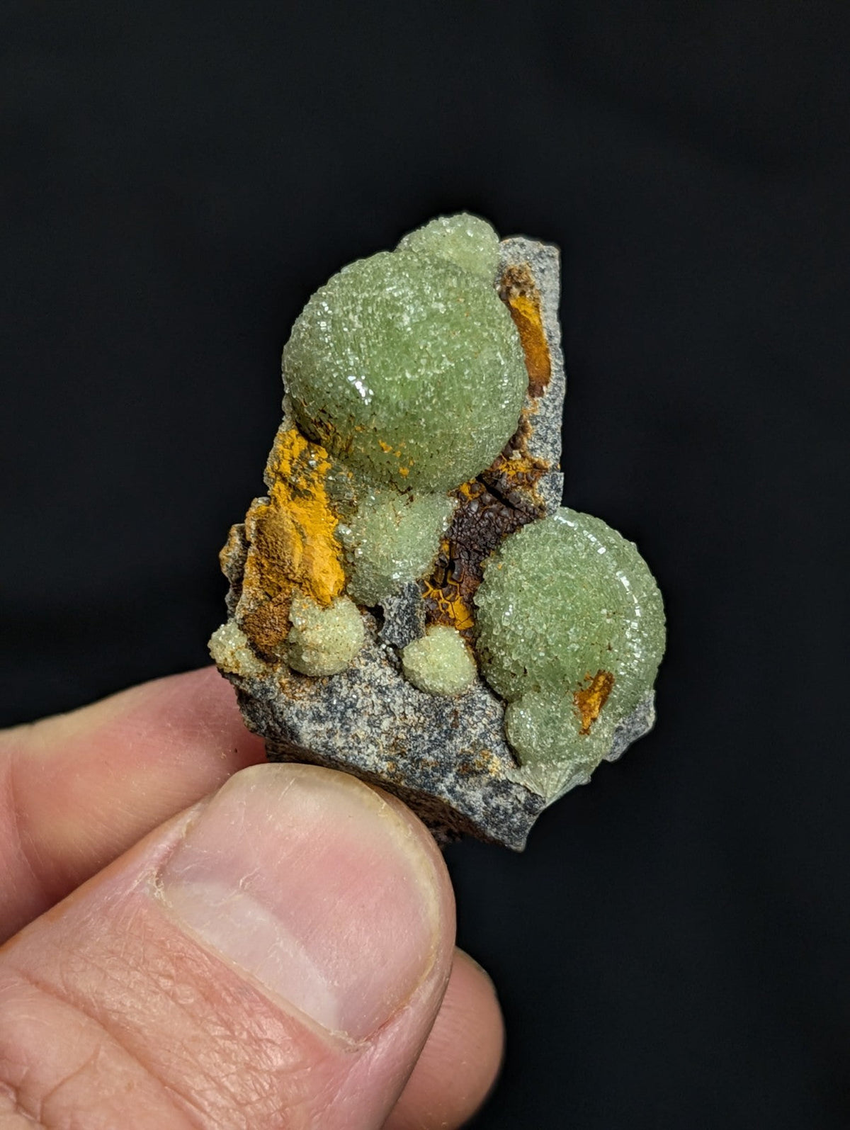 A green, rounded mineral specimen with orange and gray matrix.