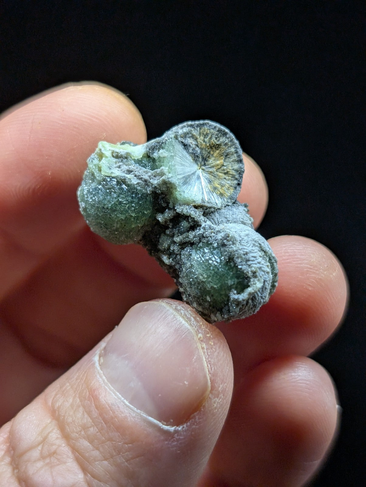 A cluster of green, translucent mineral specimens with a crystalline structure and fuzzy grayish coating.