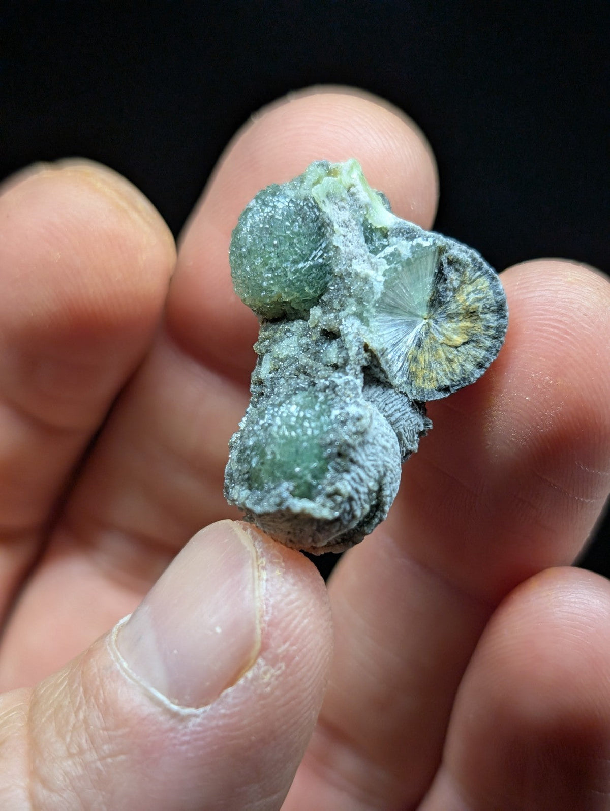 A green, crystalline mineral specimen with a rough, textured surface and translucent spherical formations.