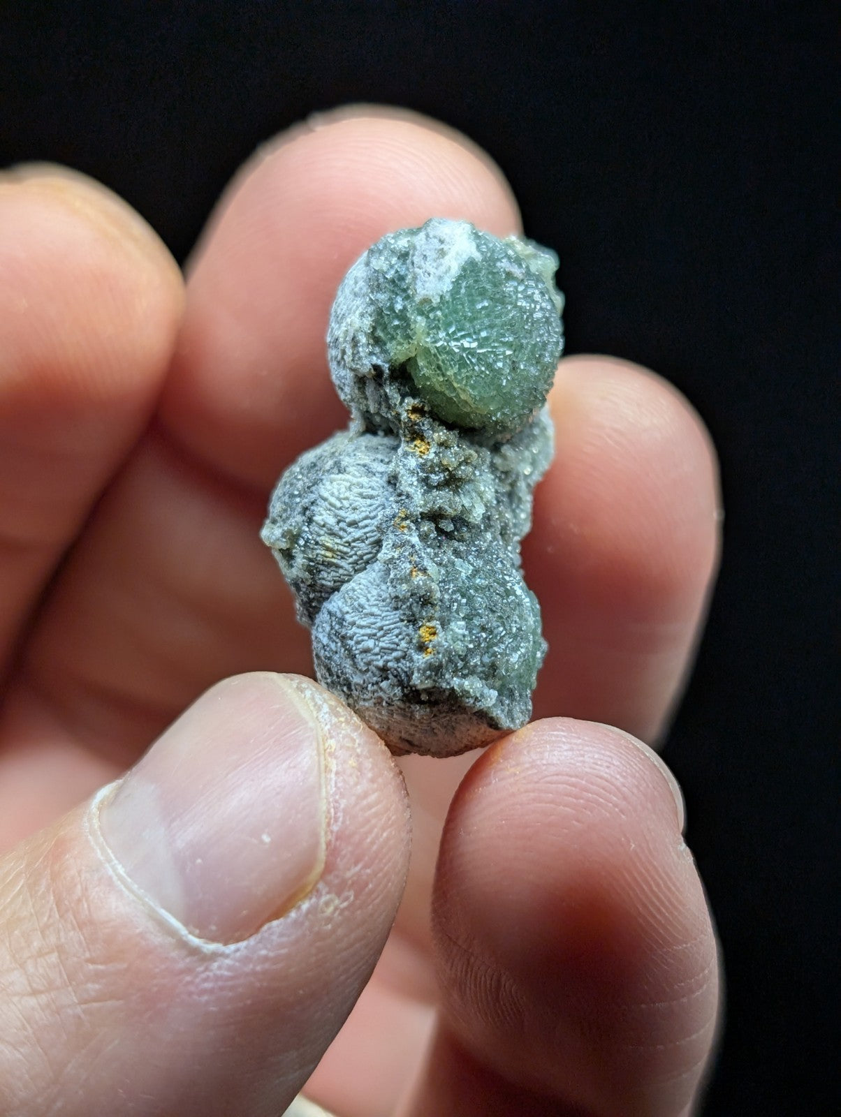 A small, textured mineral specimen with a greenish-blue crystalline formation and gray matrix.