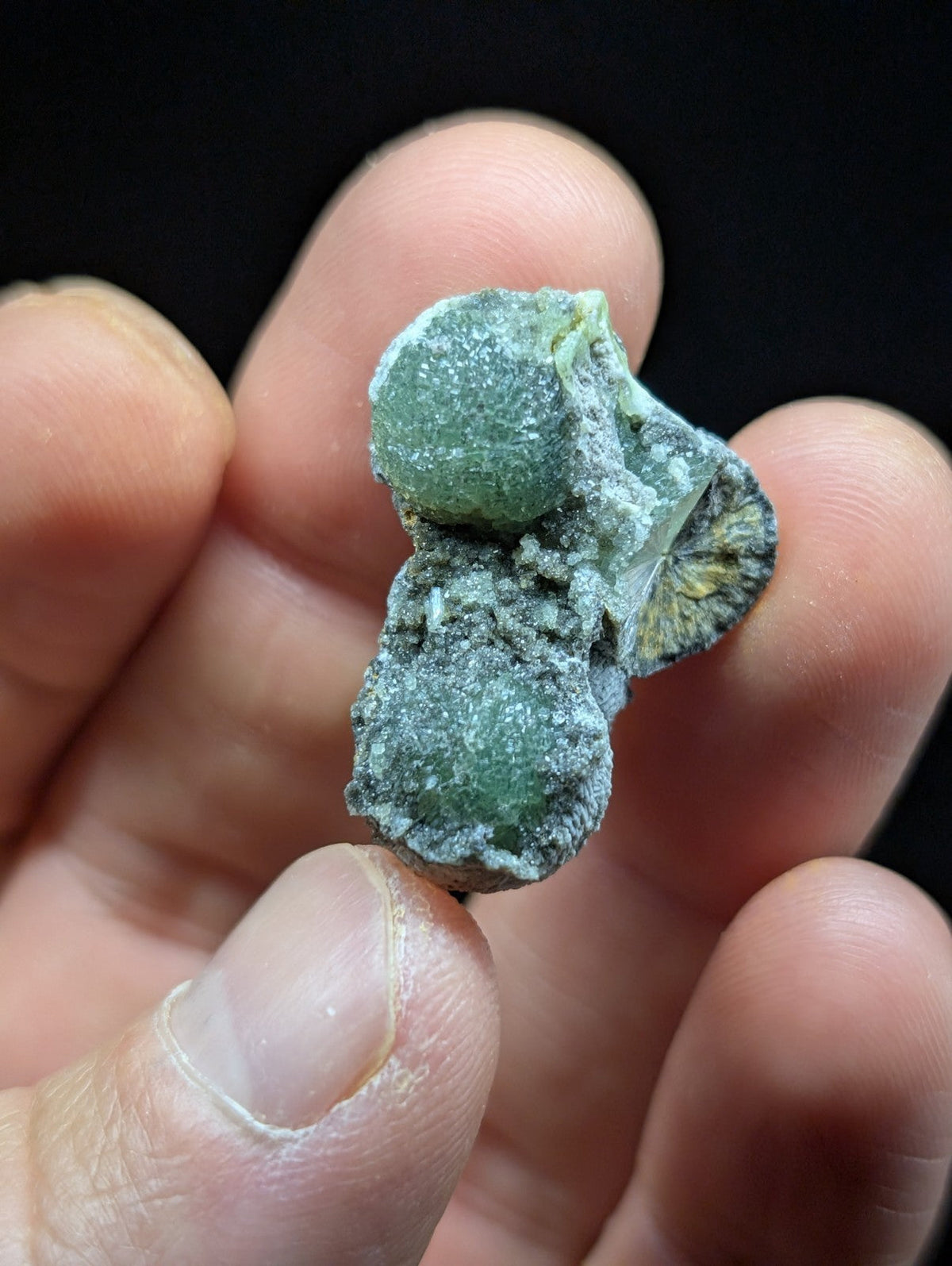 A rough, greenish mineral specimen with a textured surface and visible crystalline formations.