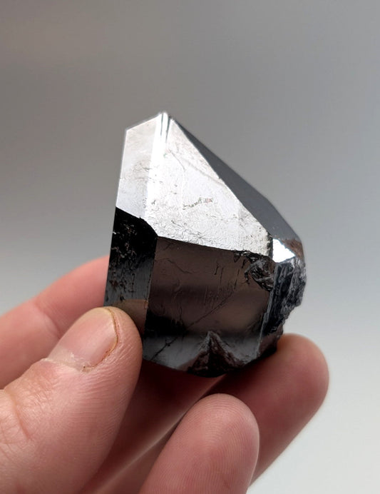 A polished, faceted black crystal with a metallic sheen and natural striations.