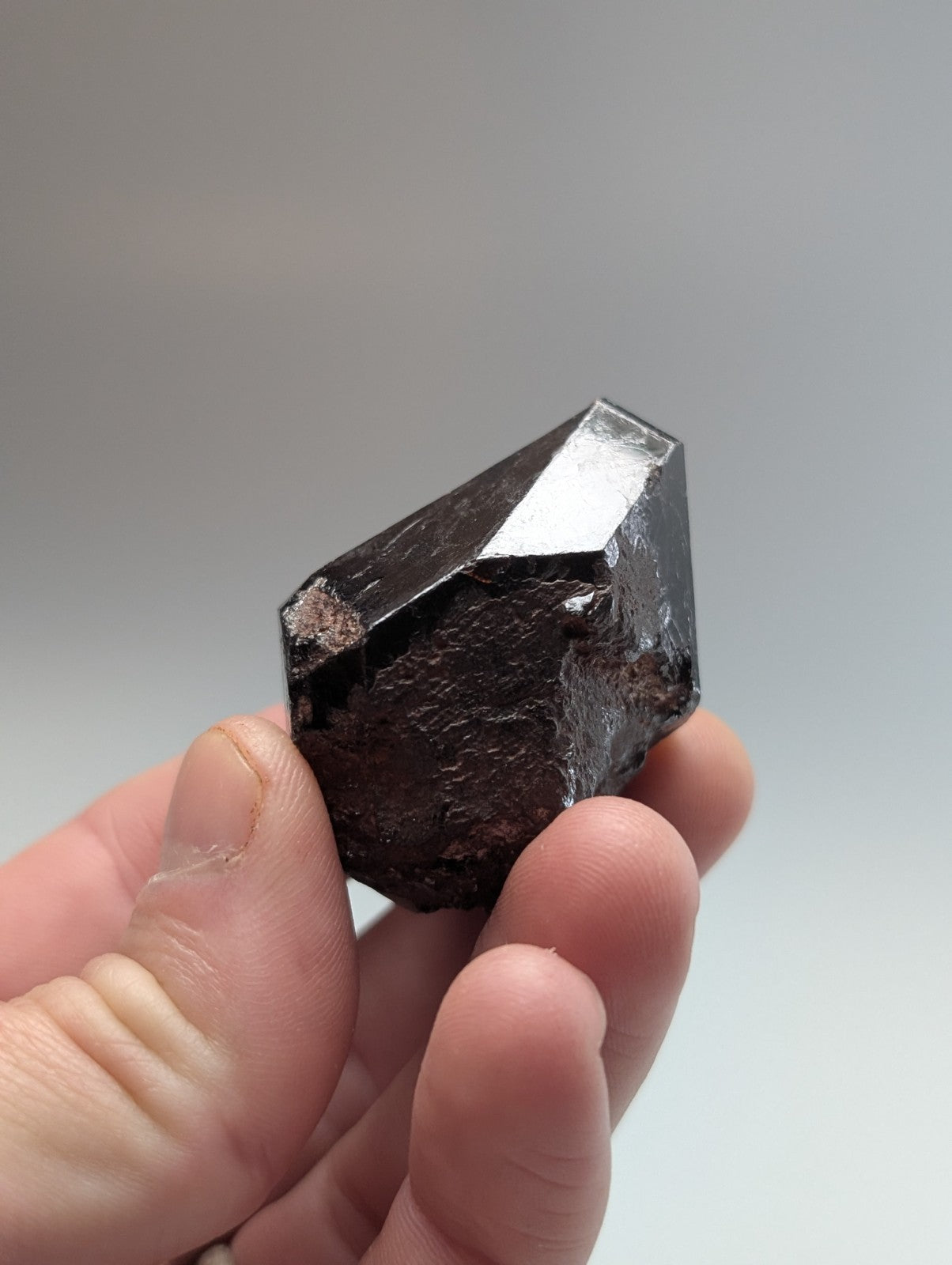 A dark, faceted mineral crystal with a glossy surface and subtle metallic sheen.