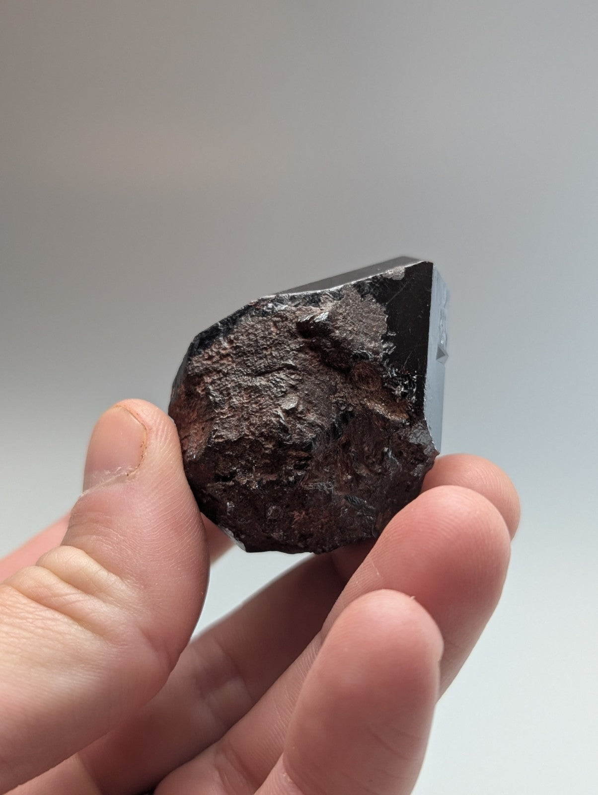 A dark, irregularly shaped meteorite with a rough, textured surface and one smooth, reflective facet.