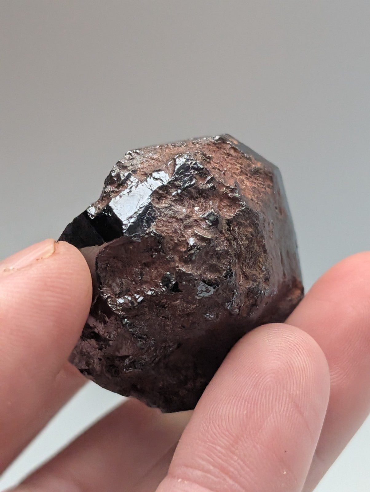 A dark, rough-textured mineral specimen with a glossy black surface and reddish-brown patches.