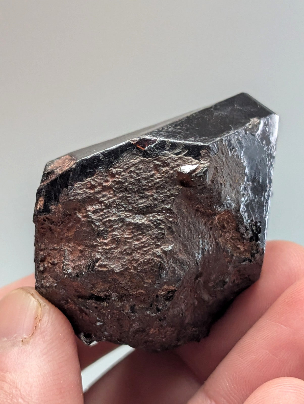 A dark, rough-textured meteorite with a metallic sheen and patches of reddish-brown mineral coating.
