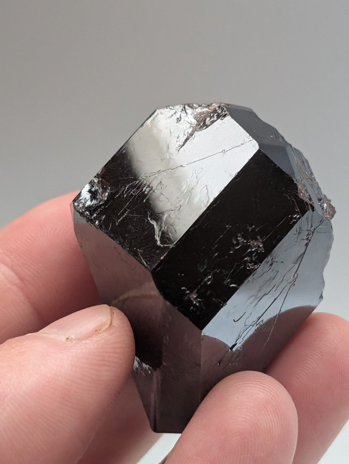 A polished, dark black tourmaline crystal with a faceted geometric shape and subtle internal striations.