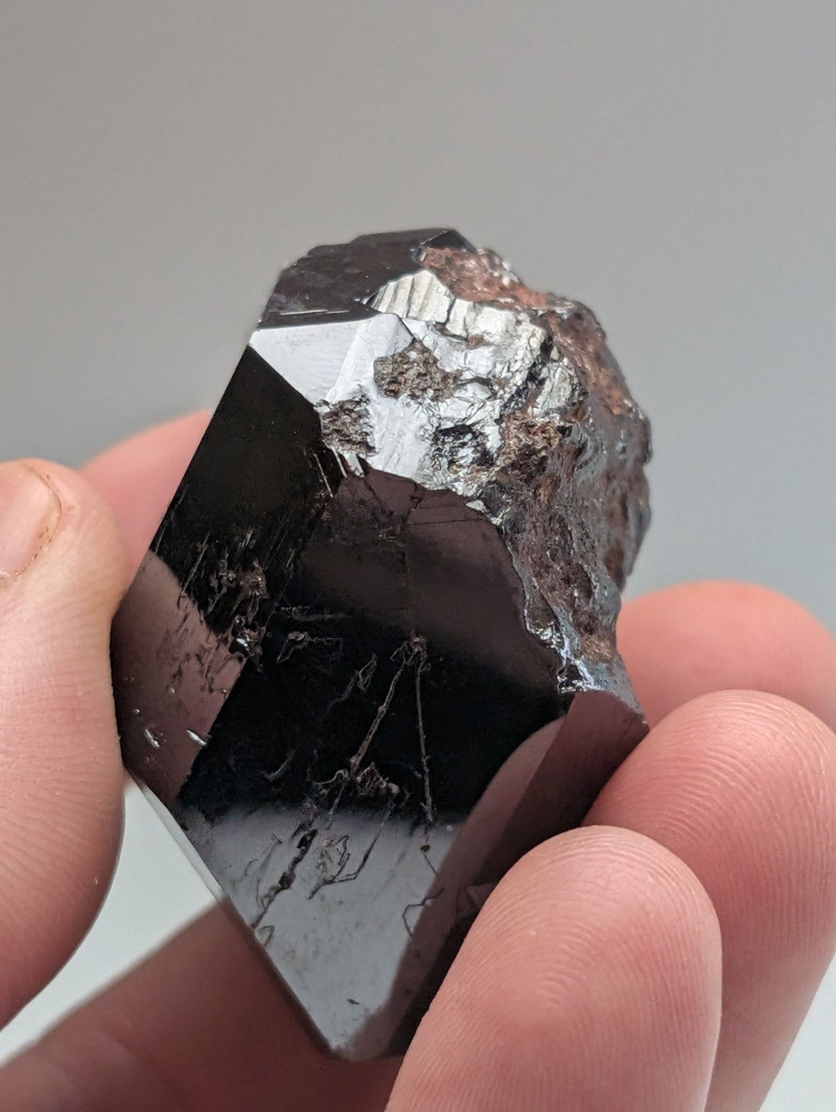 A hand holds a dark, faceted black tourmaline crystal with reflective surfaces and subtle internal veining.