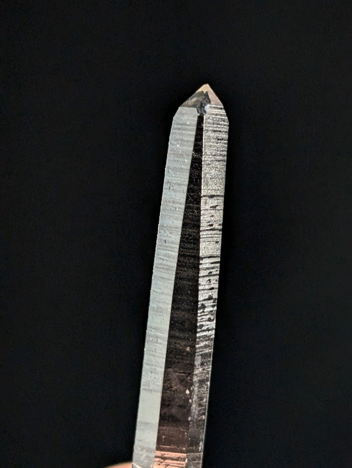 A clear quartz crystal with a pointed tip and visible internal striations, showcasing natural translucency against a dark background.