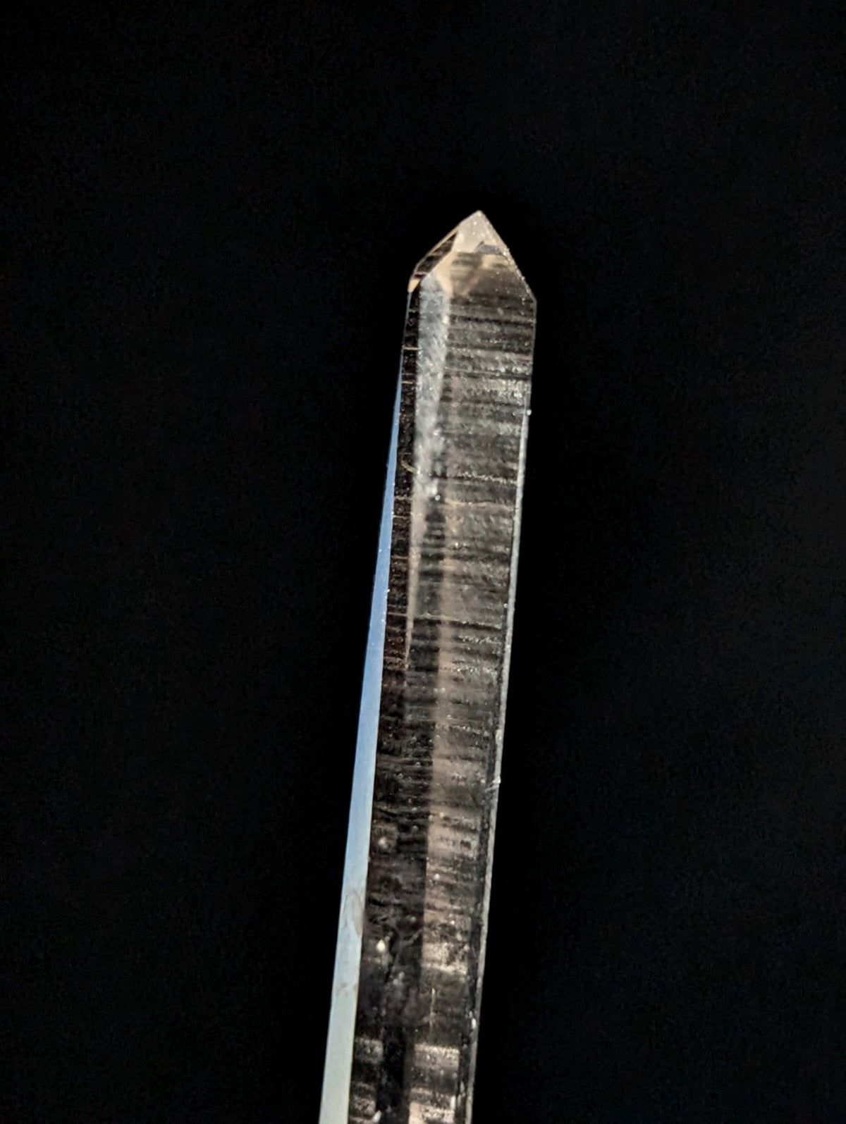 A clear, translucent quartz crystal with a pointed tip and visible internal striations.