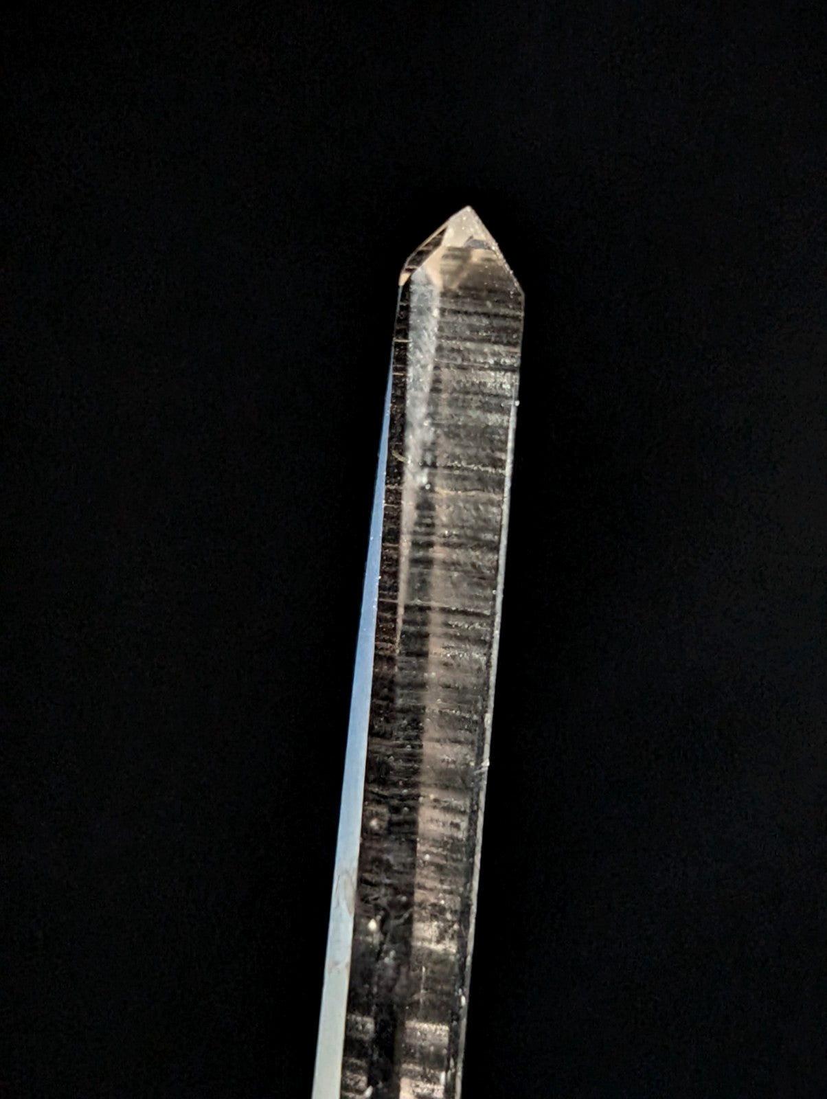 A clear, translucent quartz crystal with a pointed tip and visible internal striations.