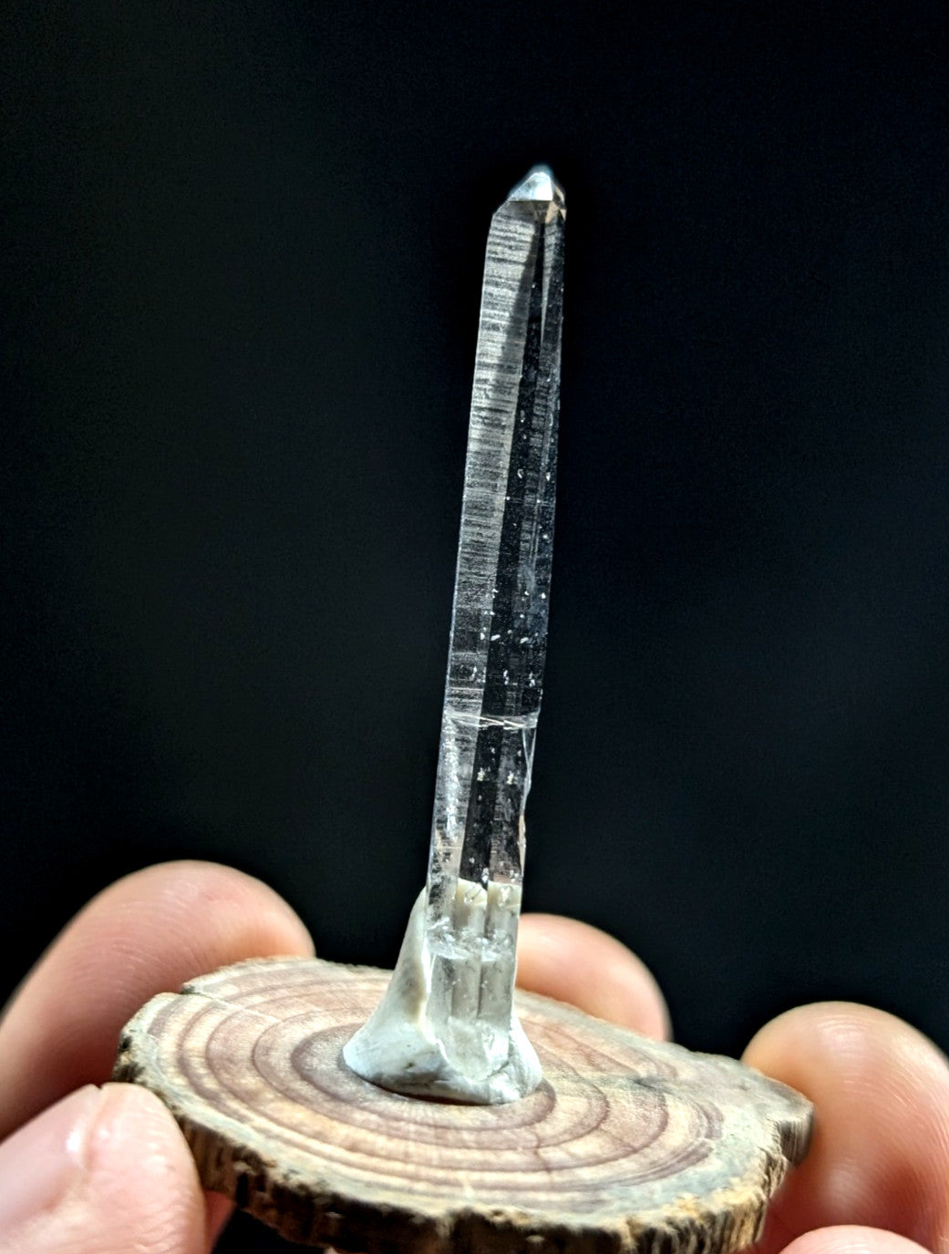 A clear, translucent quartz crystal with visible internal striations stands upright on a rustic wooden base.