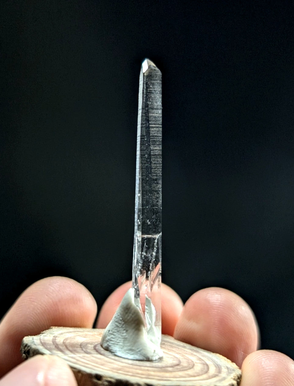A clear, transparent quartz crystal with a pointed tip and visible internal striations stands upright on a small wooden base.